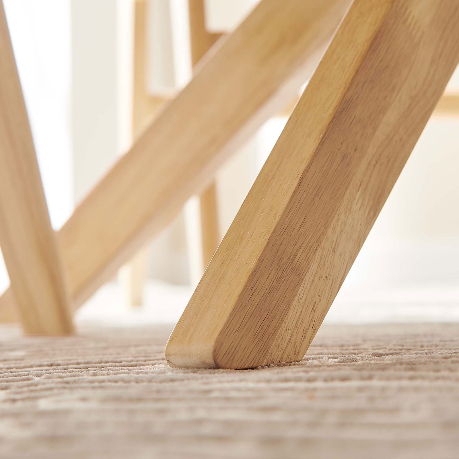 Solid oak legs rest on a textured rug, showcasing the sturdy base and nonmarking foot pads of the 71-inch table. || EEI-3849-OAK || leg_room