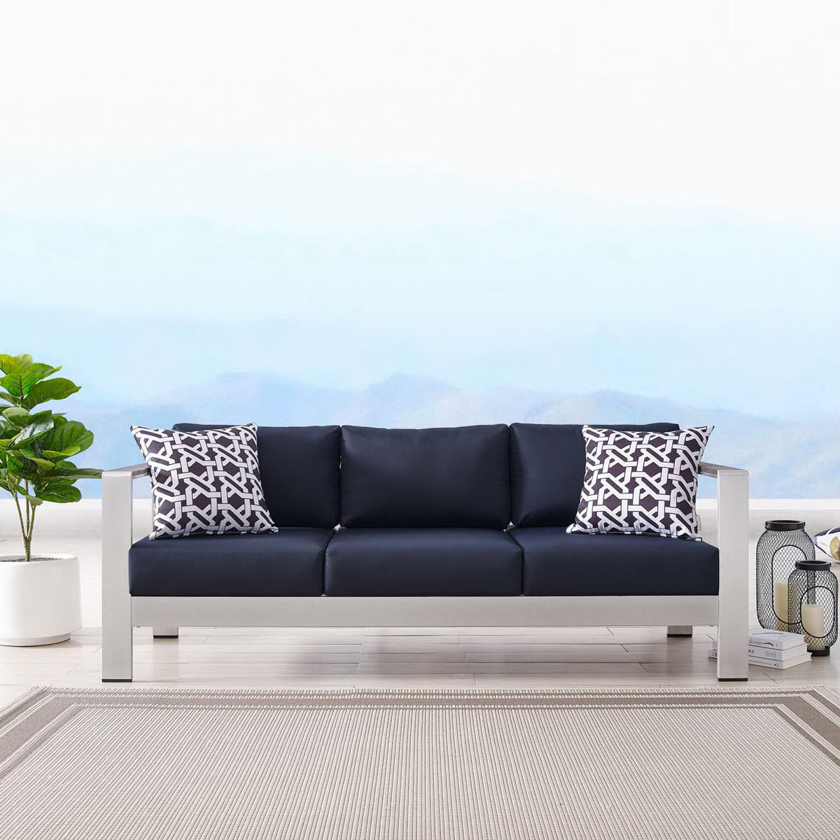 Navy cushioned sofa styled with patterned pillows, lanterns, and a neutral outdoor rug || EEI-3917-SLV-NAV || front_room