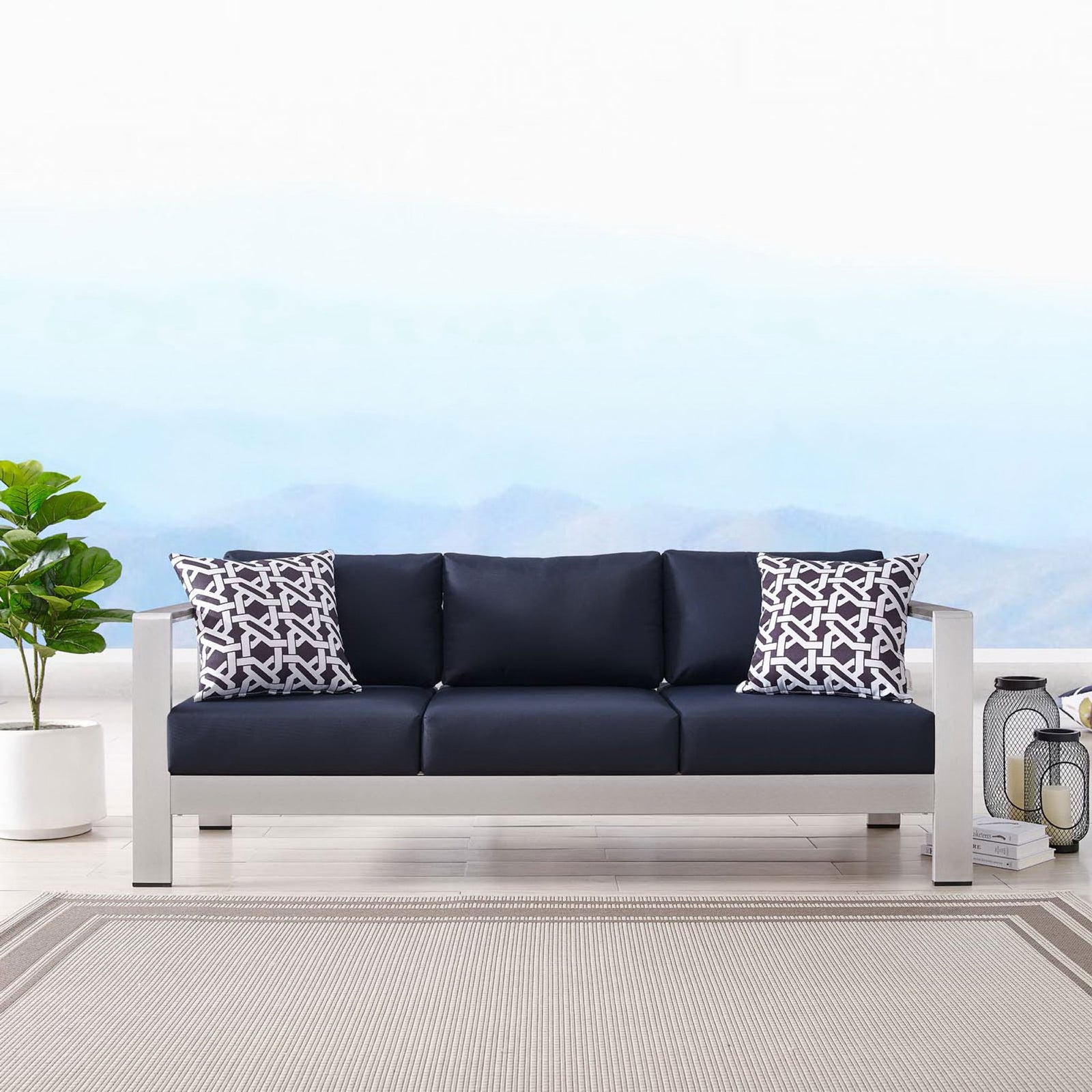 Navy cushioned sofa styled with patterned pillows, lanterns, and a neutral outdoor rug || EEI-3917-SLV-NAV || front_room