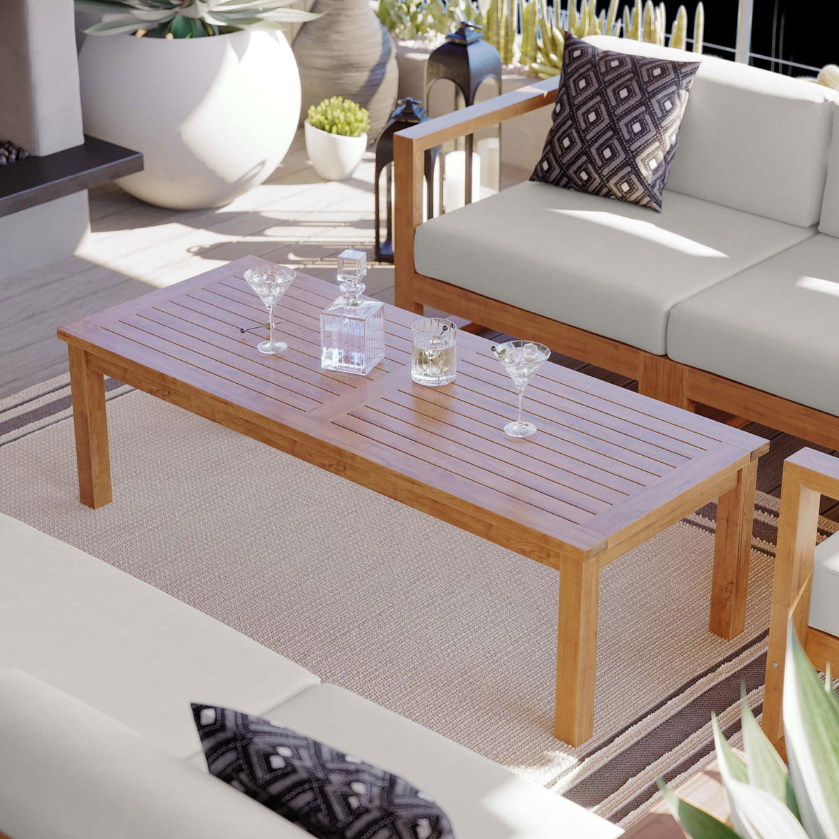 Teak outdoor coffee table styled with glassware on a patio, bringing warm wood tones to a modern seating set || EEI-4122-NAT || front_angle_room