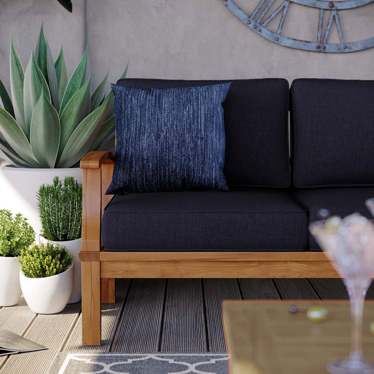 Teak patio sofa corner with navy cushions, textured throw pillow, and potted greenery accents || EEI-4176-NAT-NAV || detail_room
