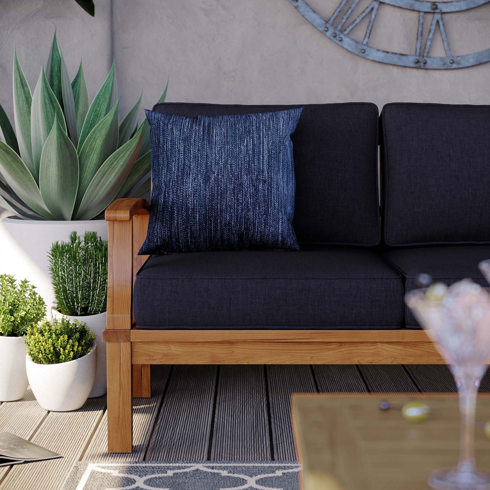Teak patio sofa corner with navy cushions, textured throw pillow, and potted greenery accents || EEI-4176-NAT-NAV || detail_room