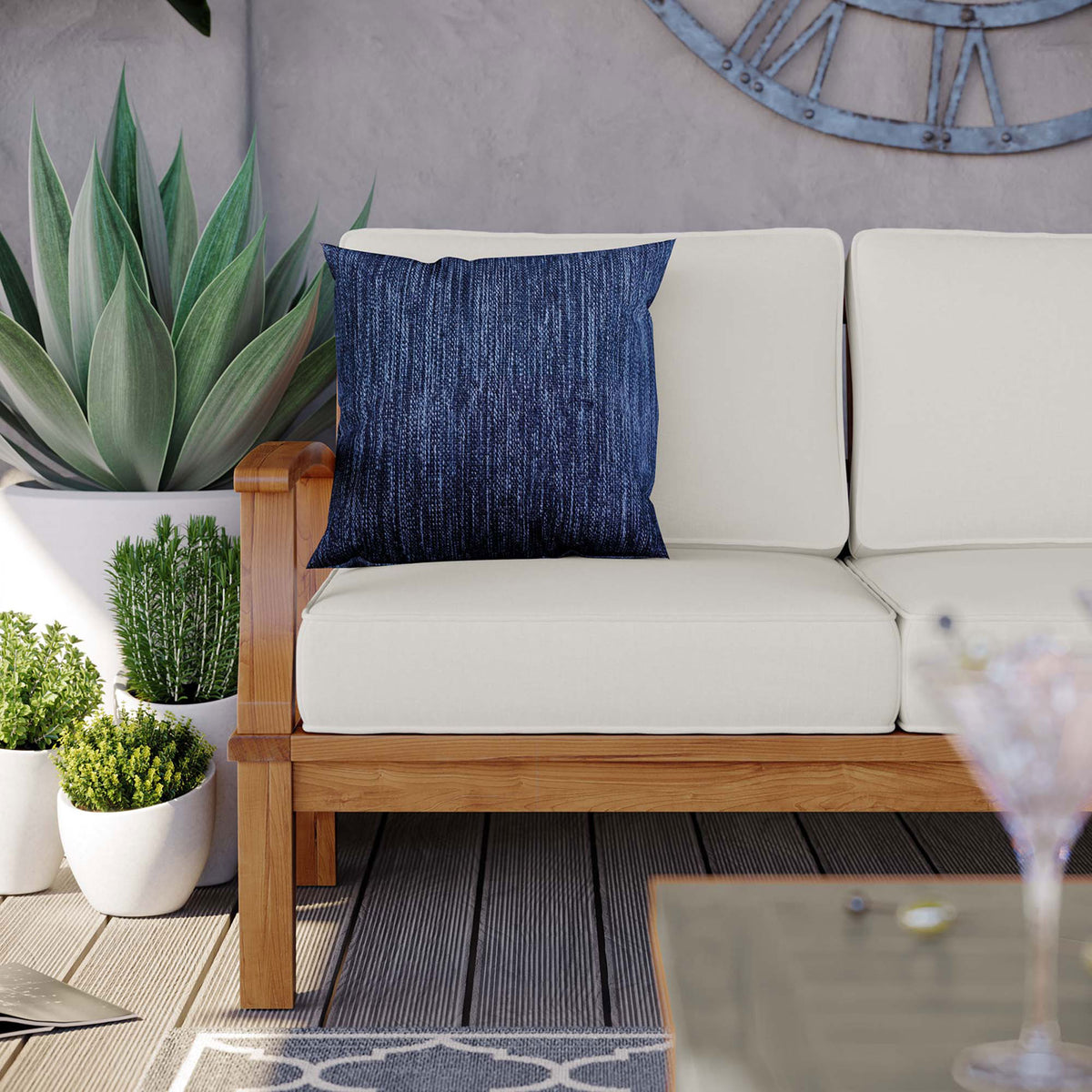 Teak patio sofa corner with white cushions, blue throw pillow, and lush potted plants || EEI-4176-NAT-WHI || detail_room