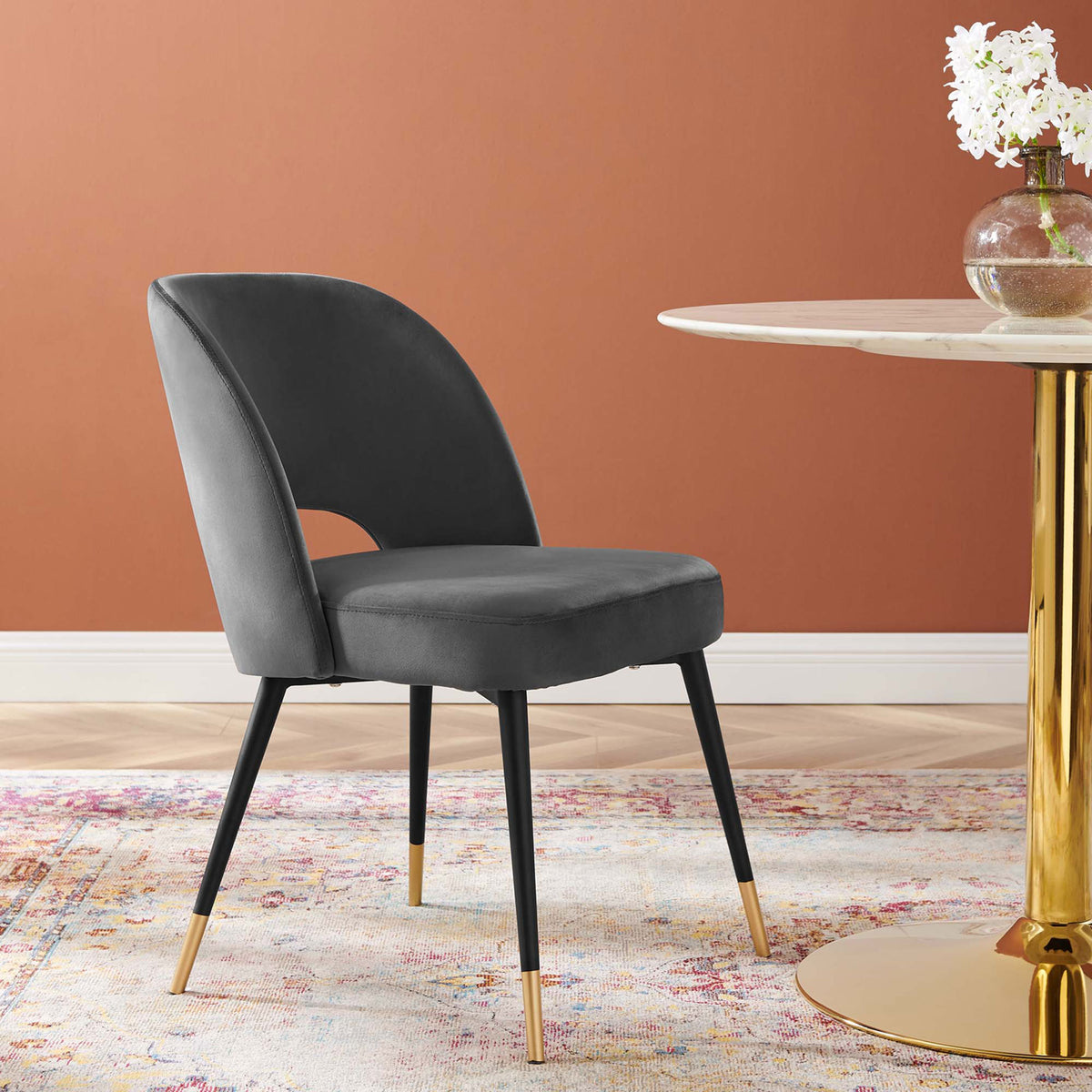 Charcoal velvet dining chair with curved back and gold-tipped legs beside a round dining table. || EEI-4212-CHA || front_angle_room