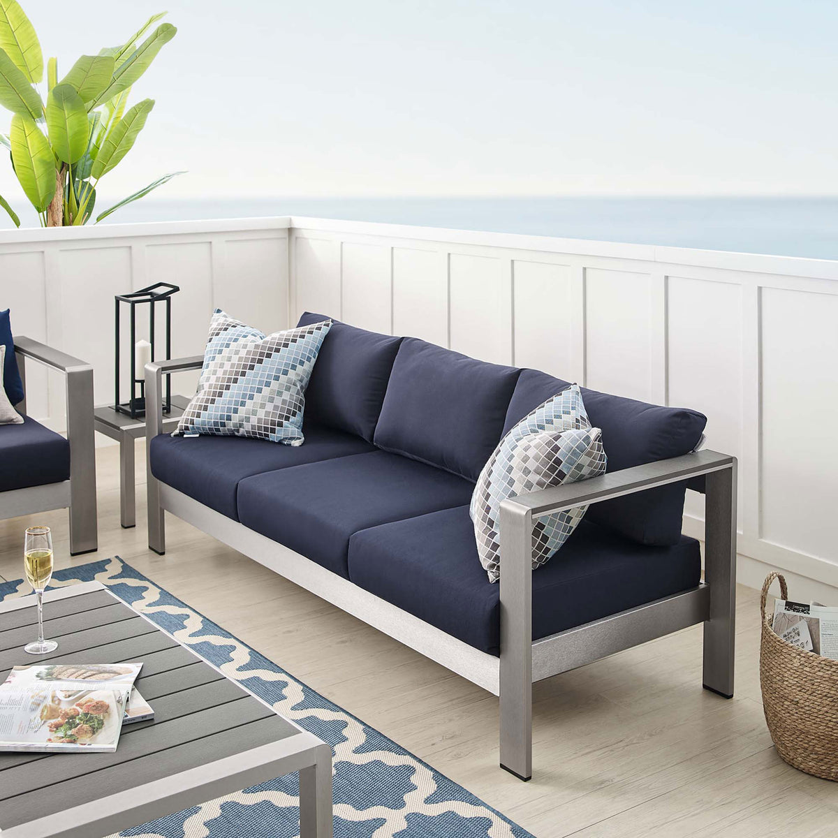 Navy cushioned Shore sofa completes a coastal-inspired patio with light flooring and blue rug accents || EEI-4228-SLV-NAV || front_angle_room
