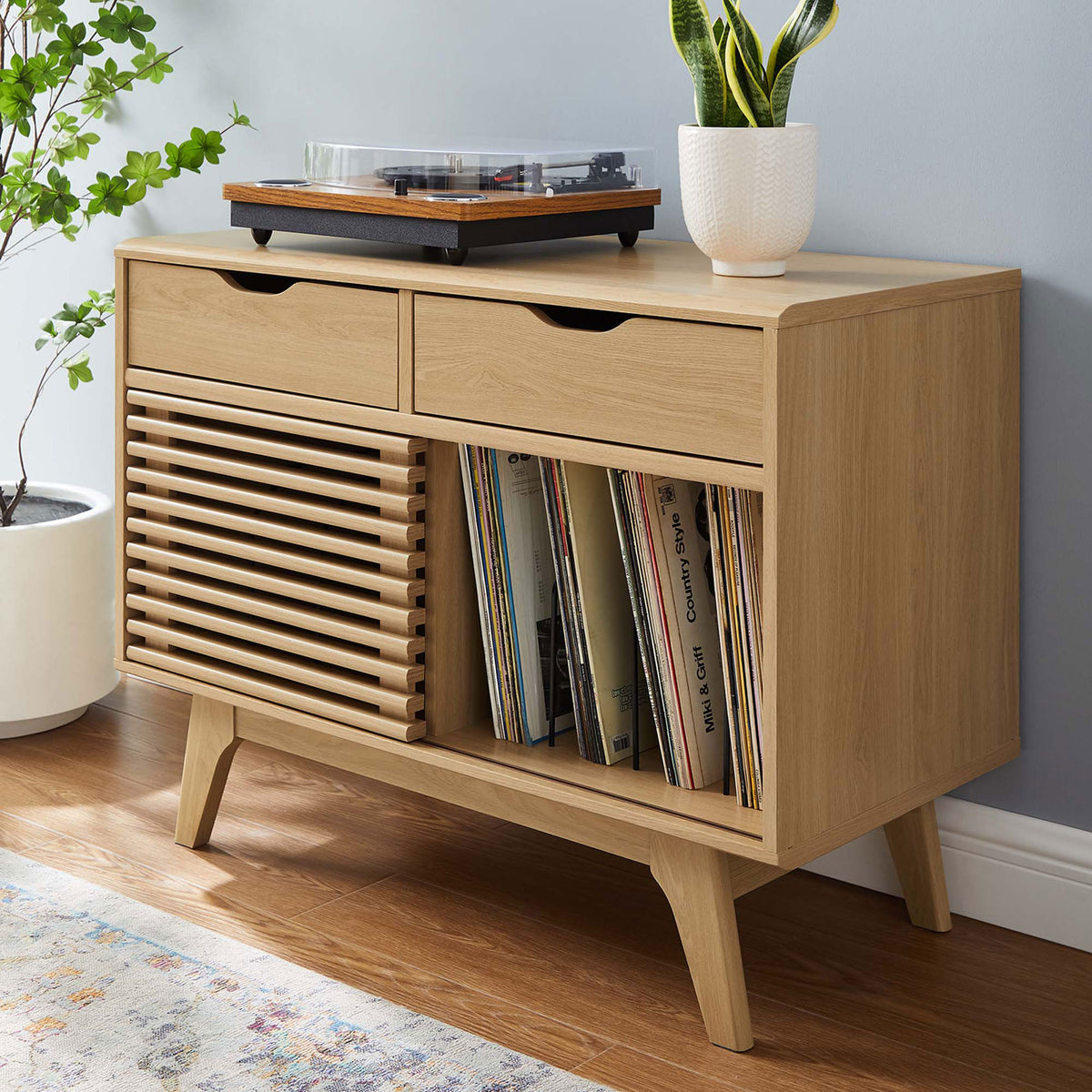 Oak record stand styled with a turntable and decor in a bright room, showcasing its warm finish and record storage || EEI-4323-OAK || front_angle_room