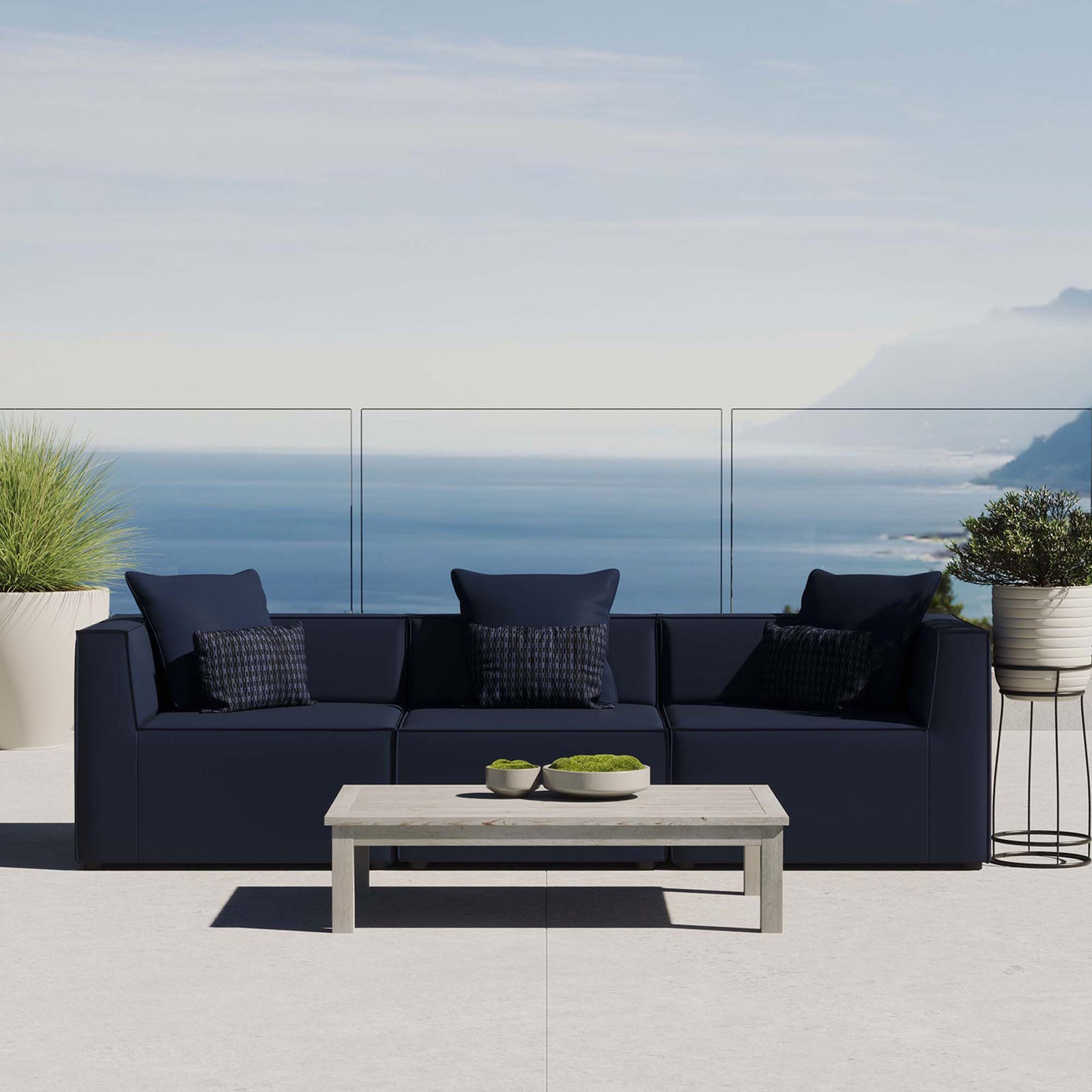 Navy outdoor sectional sofa with accent pillows arranged on a contemporary patio by the sea. || EEI-4379-NAV || front_room