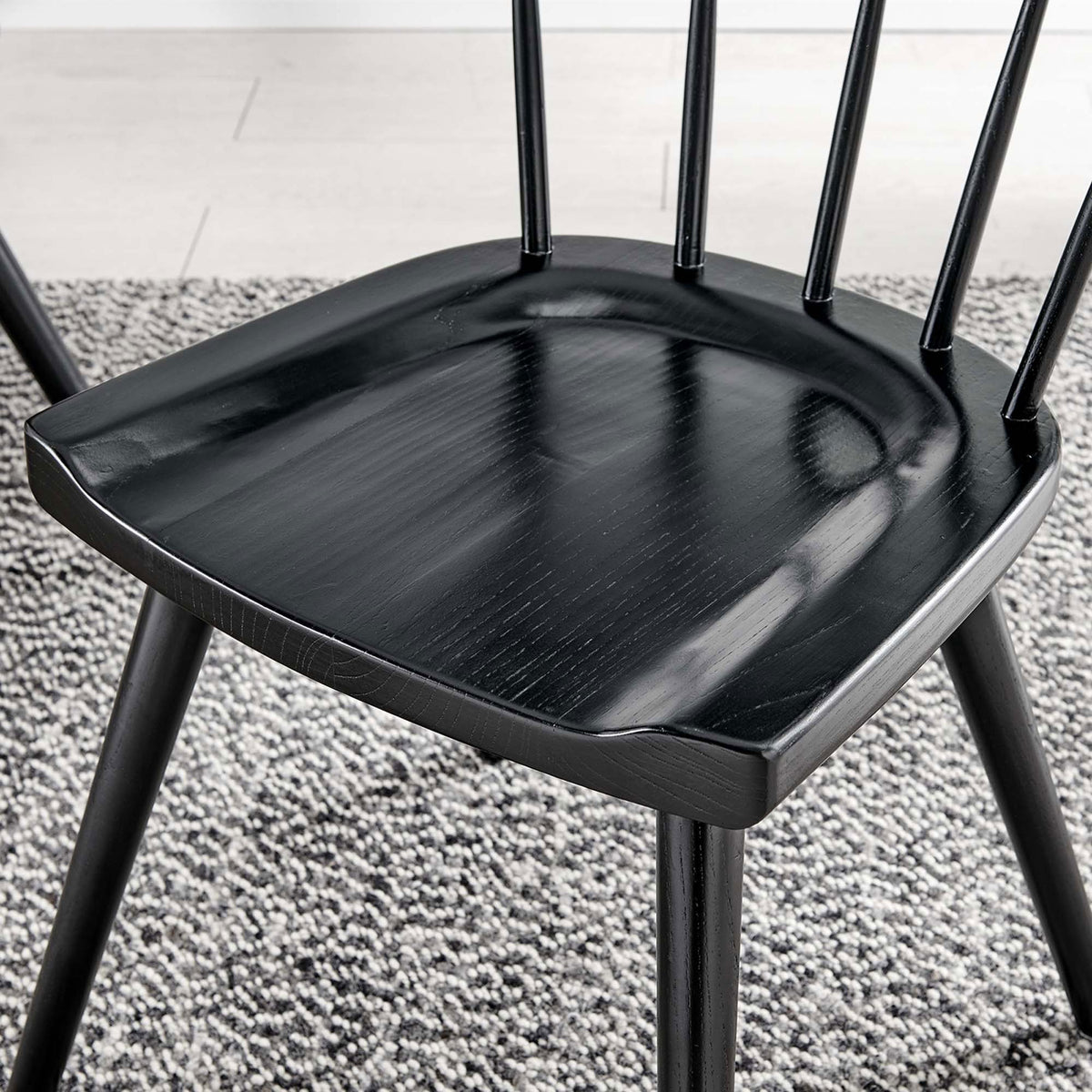 Black wood seat over a textured neutral rug, showing the chair's molded contours and soft sheen. || EEI-4650-BLK || detail_room