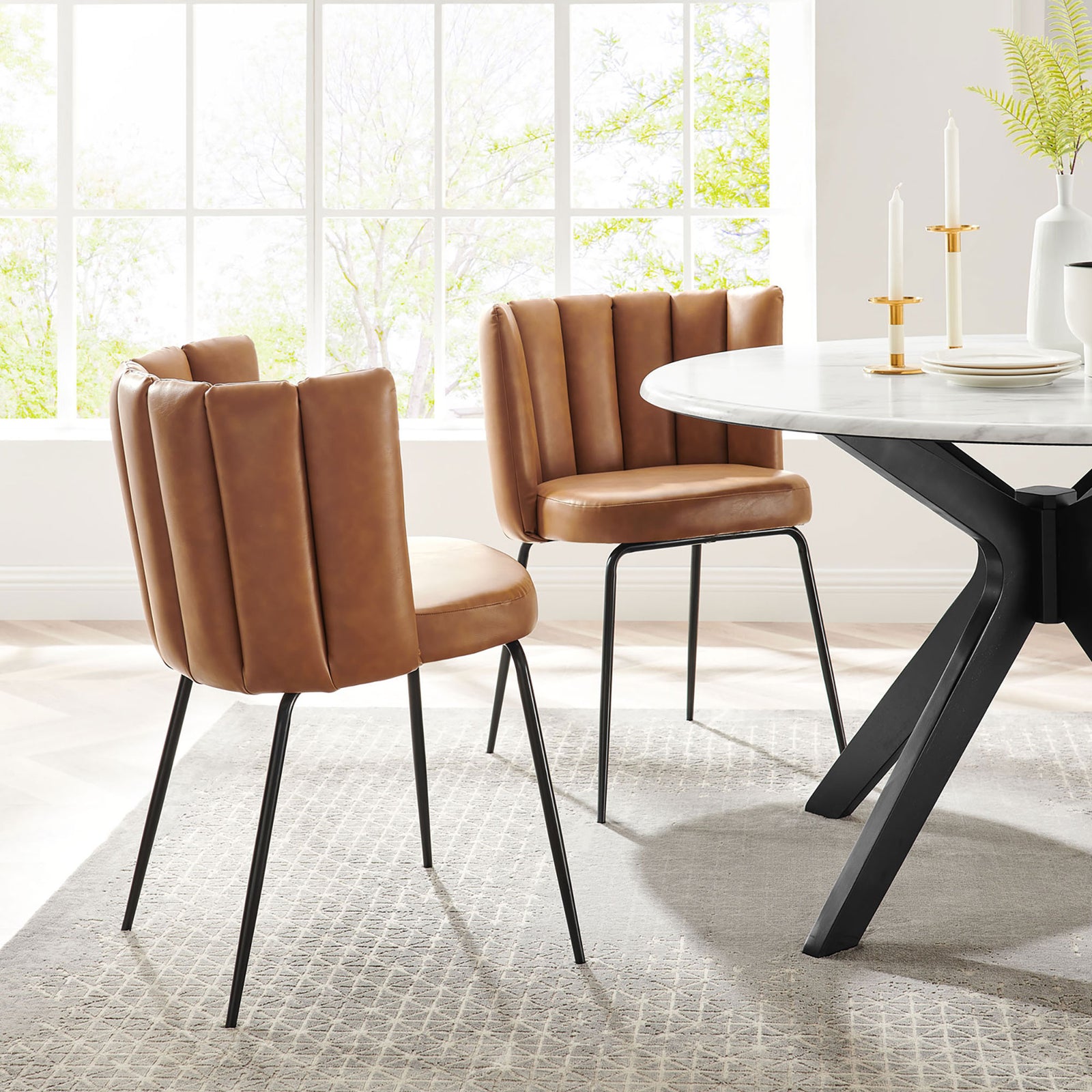 Pair of tan vegan leather dining chairs with channel-tufted backs styled around a modern round dining table || EEI-4676-BLK-TAN || front_angle_multi_room