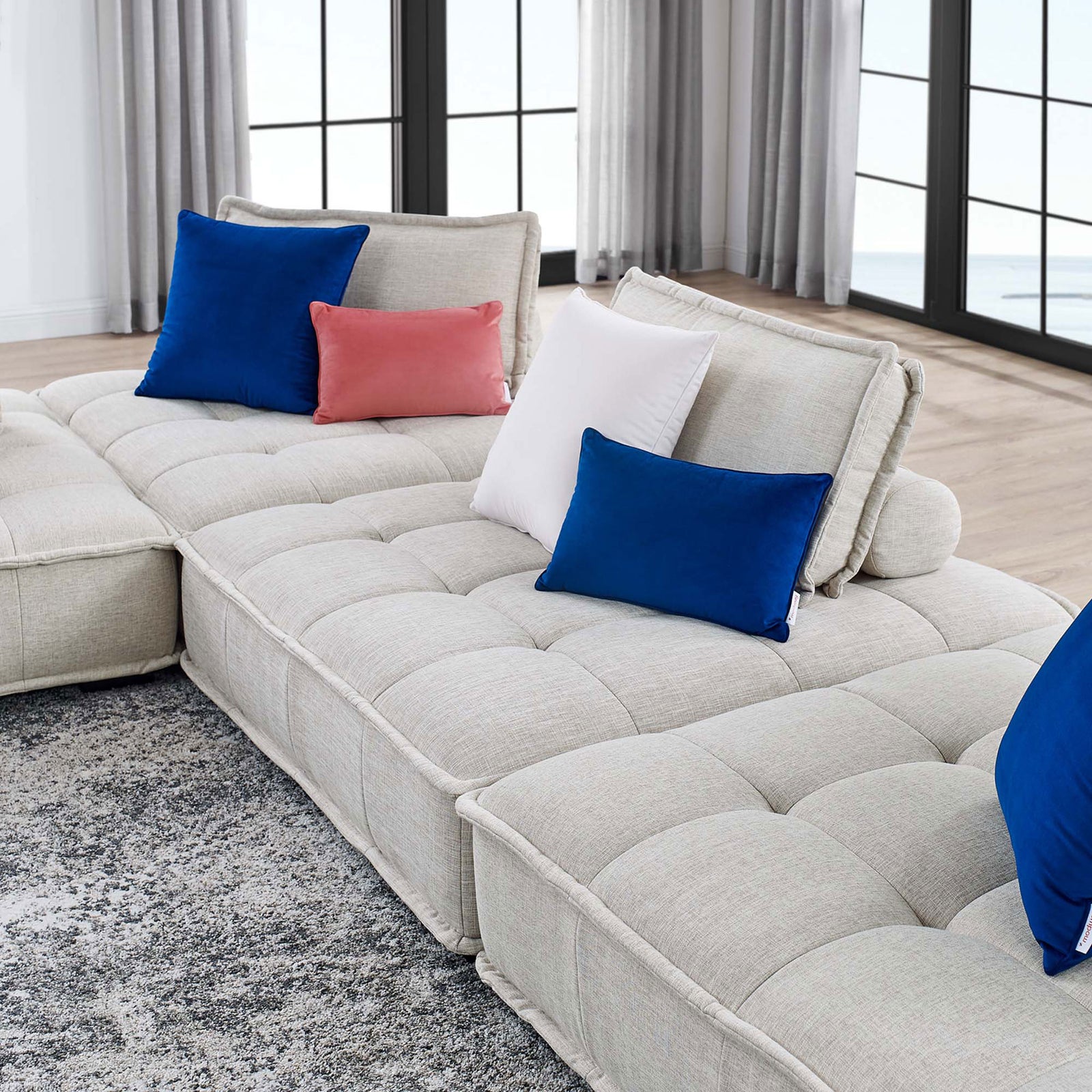 Low-profile beige sectional stretches along the living room, complemented by vibrant accent pillows and rug || EEI-5208-BEI || detail_room