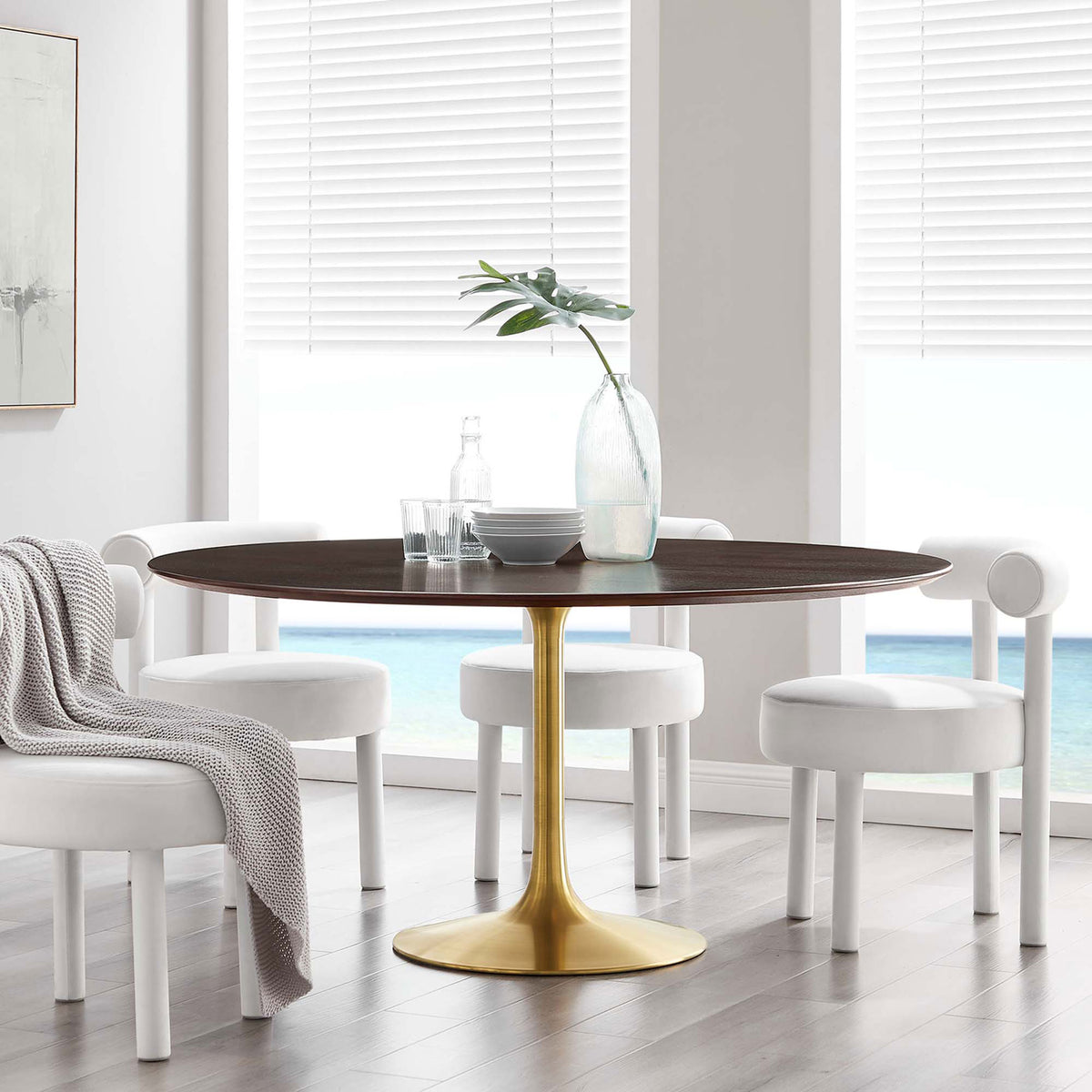 Generous round cherry walnut pedestal table with brushed gold base centered in a sunlit seaside dining room || EEI-5232-GLD-CHE || front_angle_room