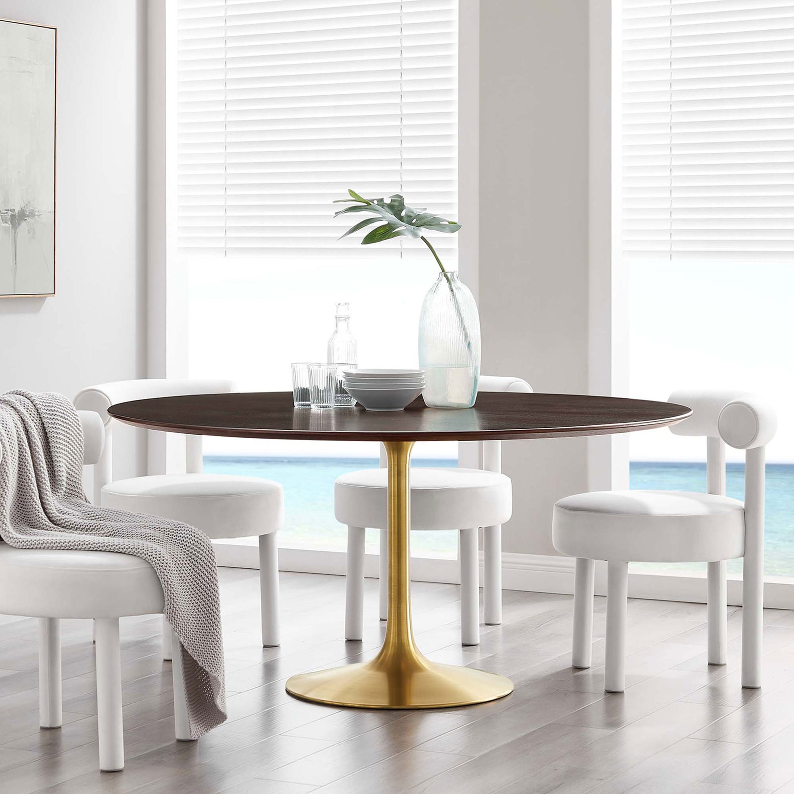 Generous round cherry walnut pedestal table with brushed gold base centered in a sunlit seaside dining room || EEI-5232-GLD-CHE || front_angle_room
