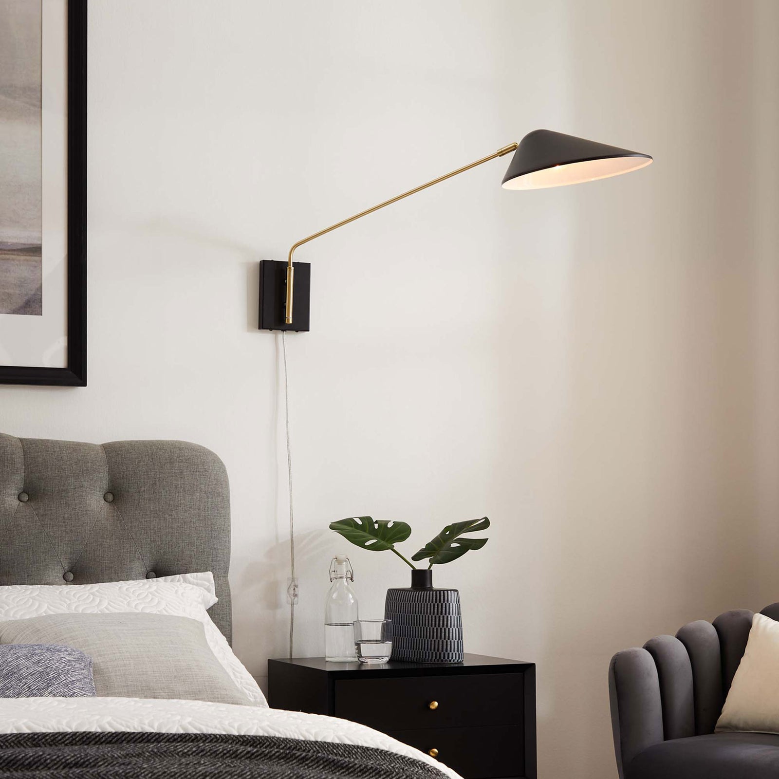 Illuminated black Journey sconce casts warm light across the bed and accent chair. || EEI-5295-BLK || front_angle_on_room