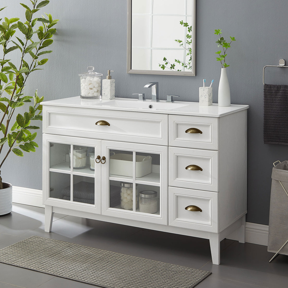 Bright vanity anchors the bath with airy glass doors, brass hardware, and a glossy ceramic basin || EEI-5427-WHI-WHI || front_angle_room