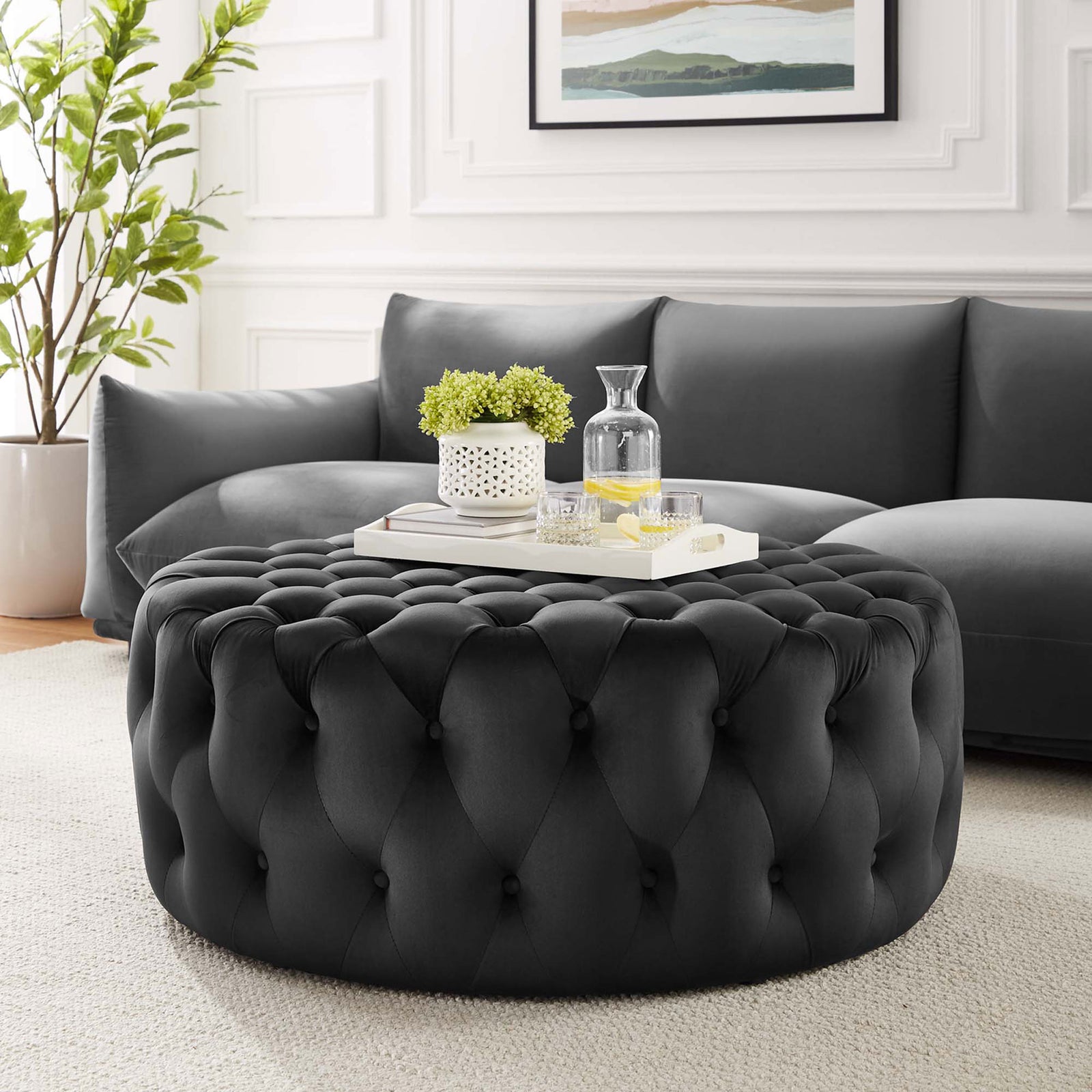 Black velvet tufted ottoman styled in a bright living room, perfect as a centerpiece and soft extra seating || EEI-5469-BLK || front_angle_room