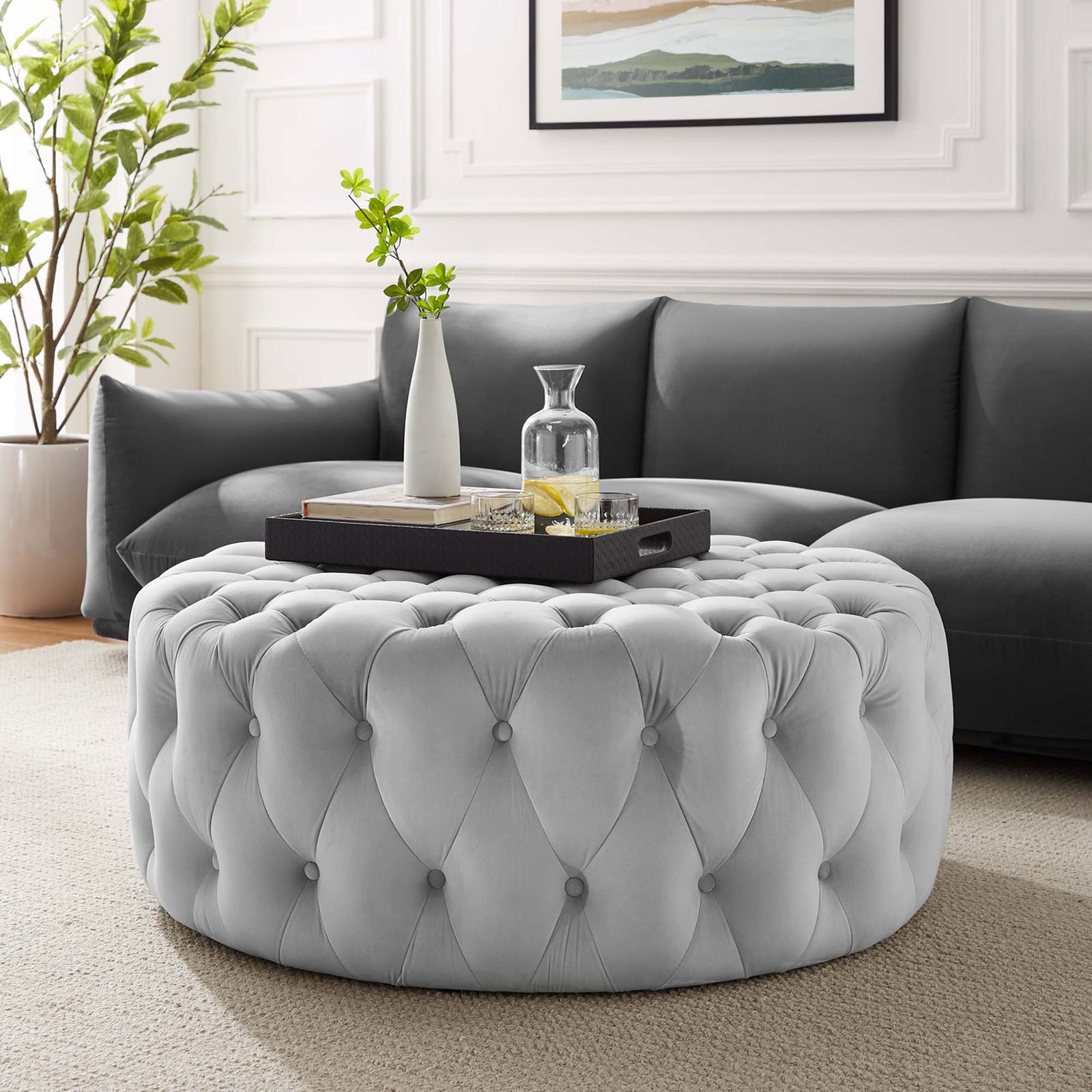 Light gray tufted round velvet ottoman styled as a chic coffee table centerpiece in a modern living room || EEI-5469-LGR || front_angle_room