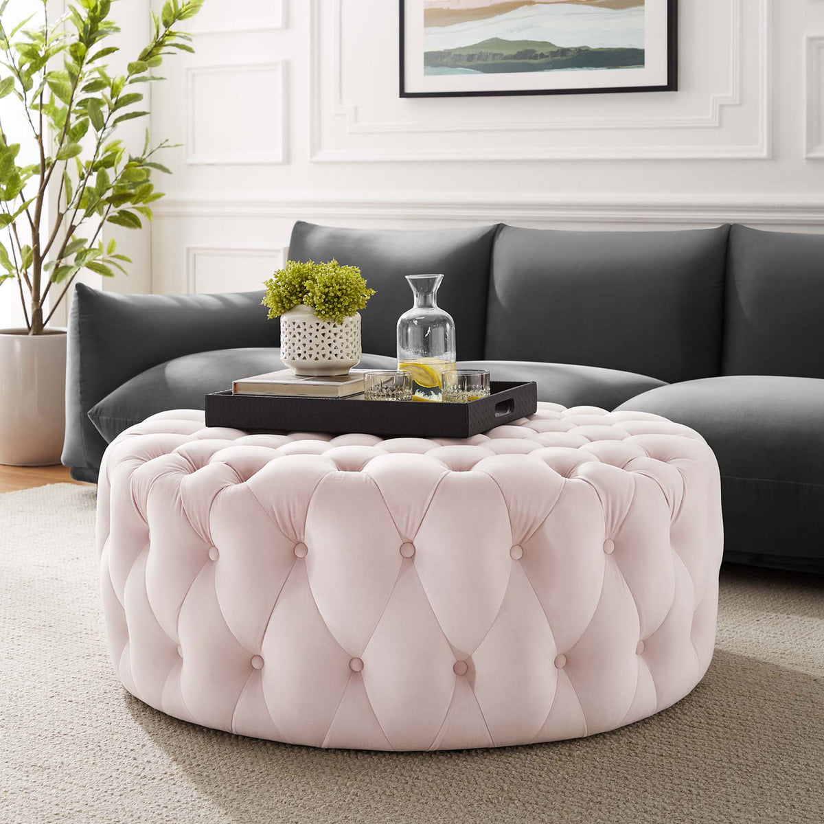 Blush pink round tufted ottoman in a modern living room styled as a coffee table || EEI-5469-PNK || front_angle_room