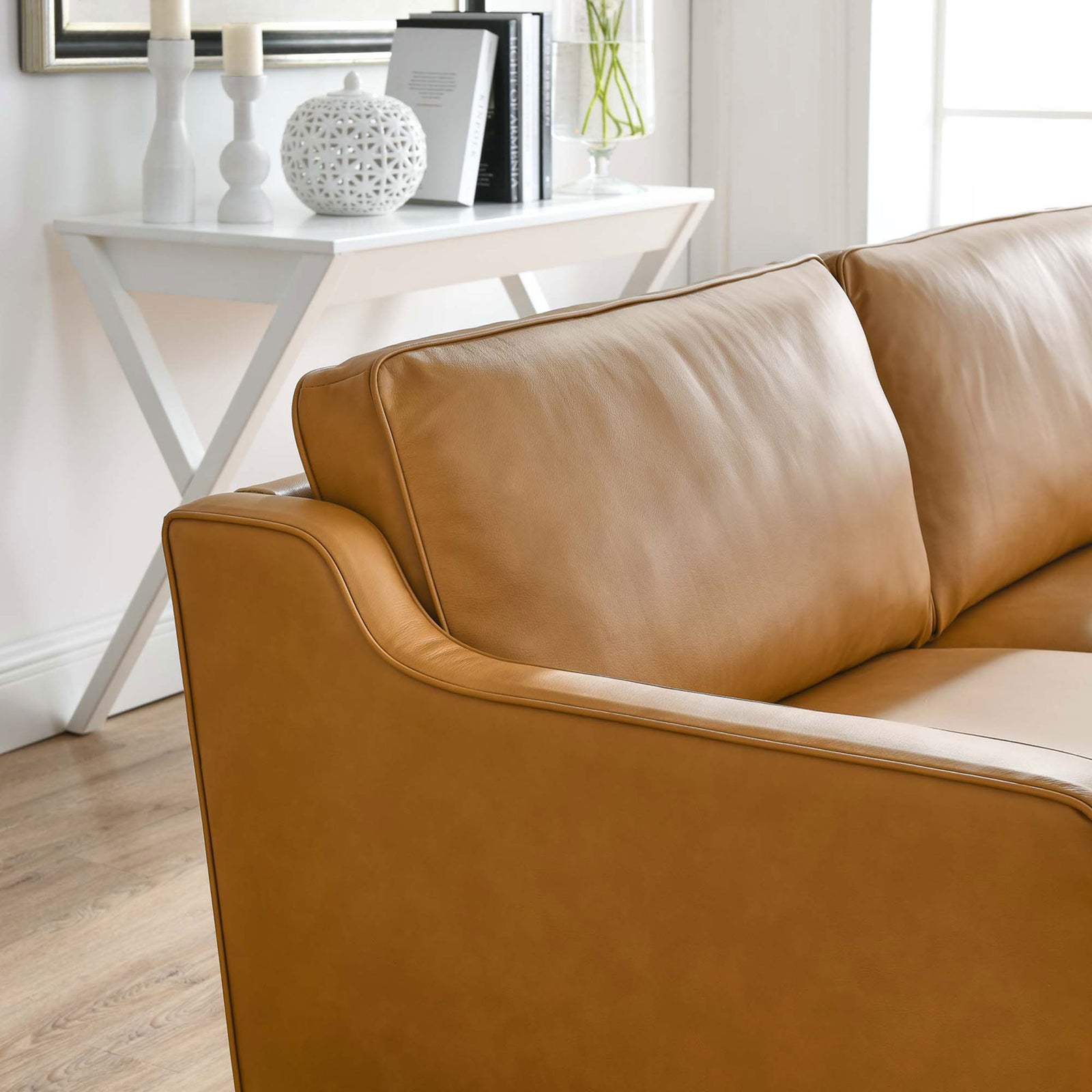 Tan leather sofa arm and cushions next to a white console table and decorative accents || EEI-5553-TAN || detail_room
