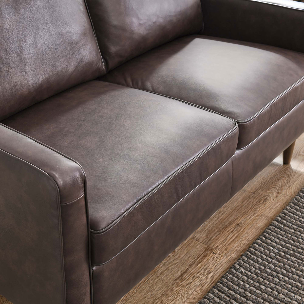 Brown leather loveseat seat cushions showing smooth upholstery and refined edge piping over wood flooring || EEI-5554-BRN || detail_room