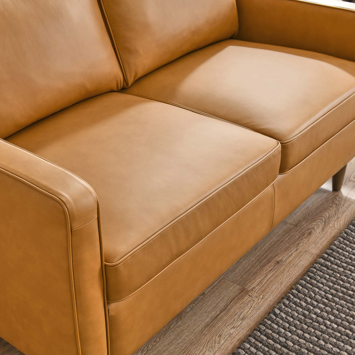 Tan leather loveseat seat cushions with smooth upholstery styled over warm wood floors and a textured rug. || EEI-5554-TAN || detail_room