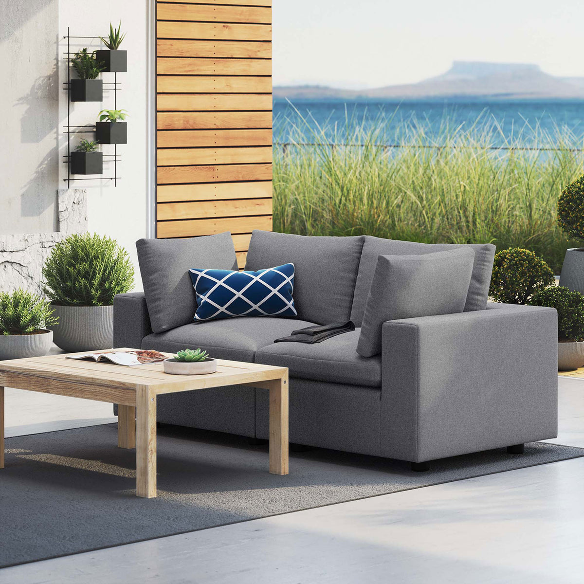 Gray outdoor loveseat on a modern patio overlooking coastal scenery with lush greenery || EEI-5577-SLA || front_angle_room