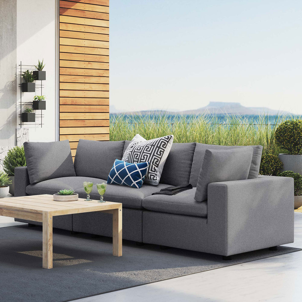 Gray Sunbrella three-seat outdoor sofa on a modern patio paired with a light wood coffee table || EEI-5579-SLA || front_angle_room