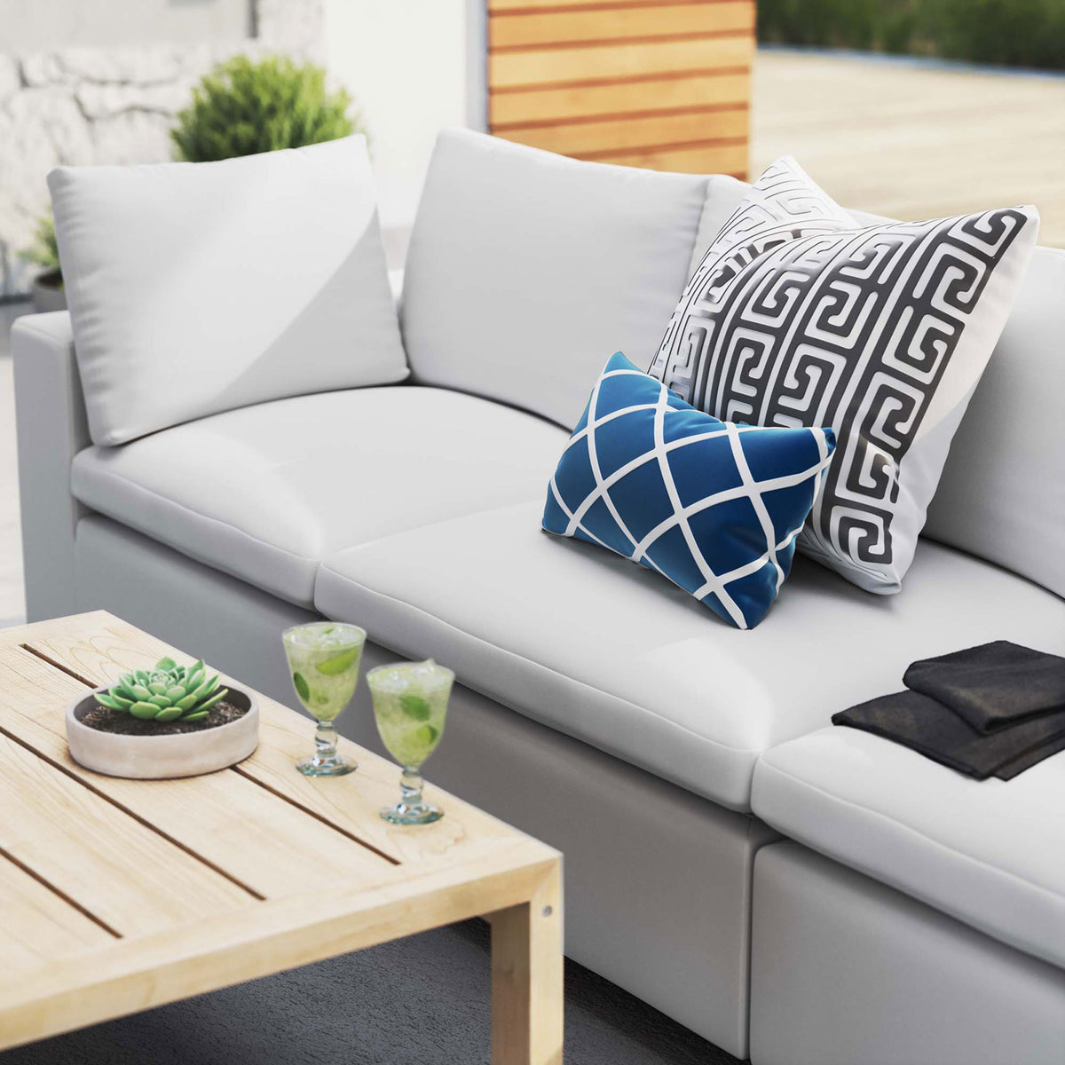 White Sunbrella outdoor sofa styled with bold accent pillows, greenery, and a wood coffee table || EEI-5579-WHI || detail_room