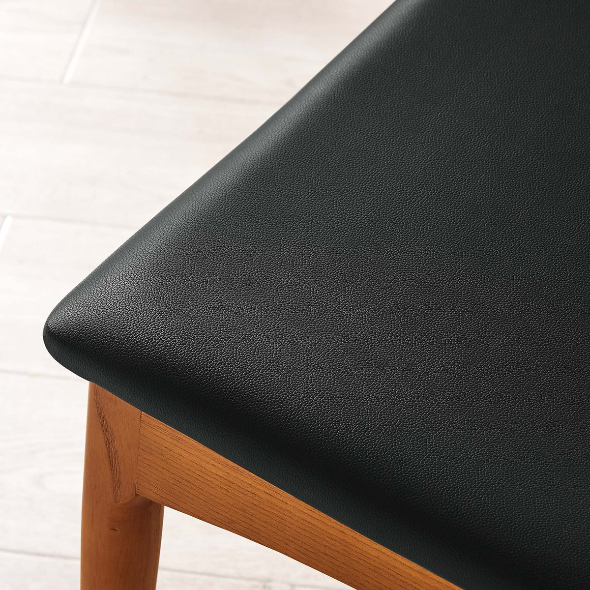 Subtly textured black faux leather wraps the padded seat above a warm wood frame.