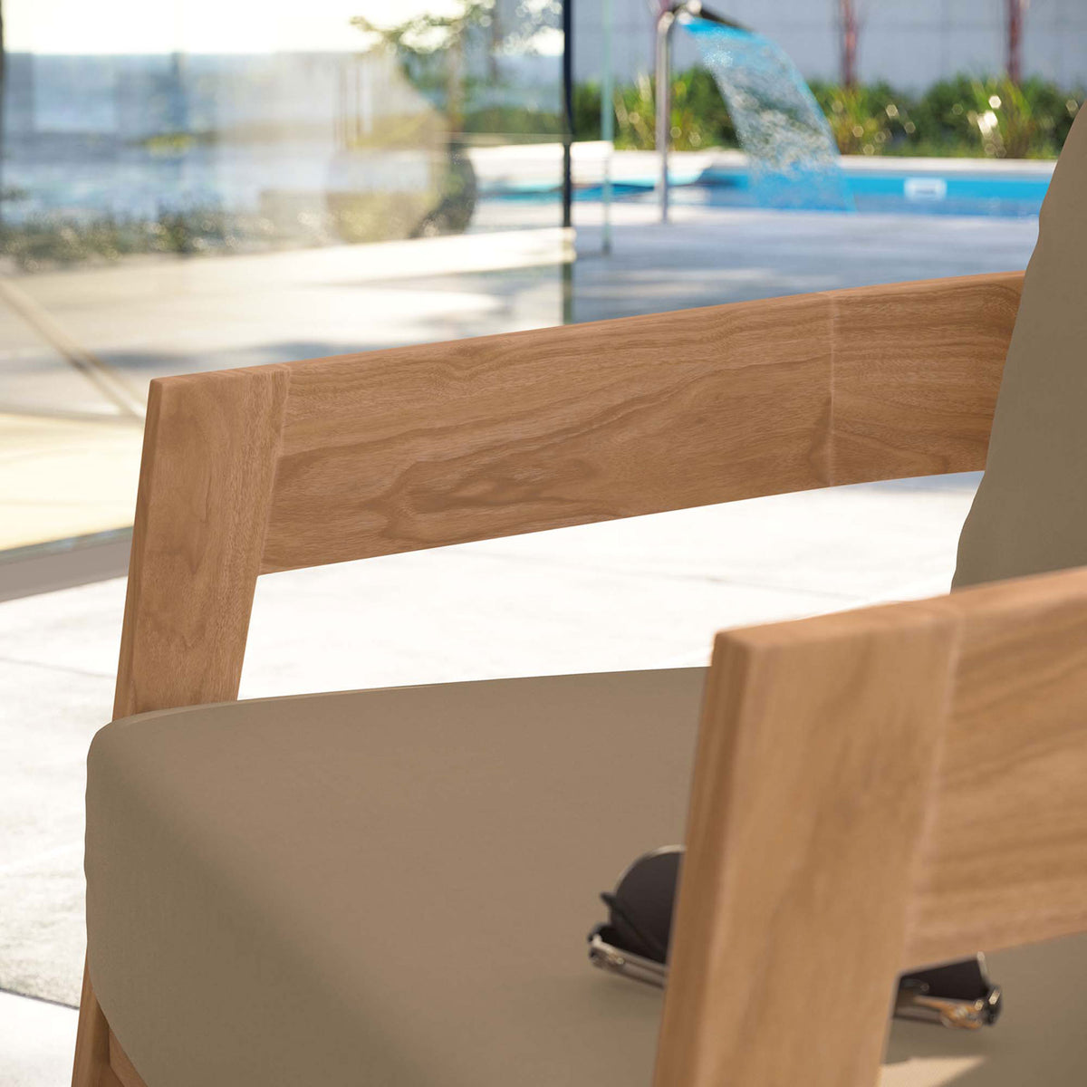 Teak arm and light brown cushion of outdoor chair styled beside a pool with modern glass architecture || EEI-5602-NAT-LBR || detail_room