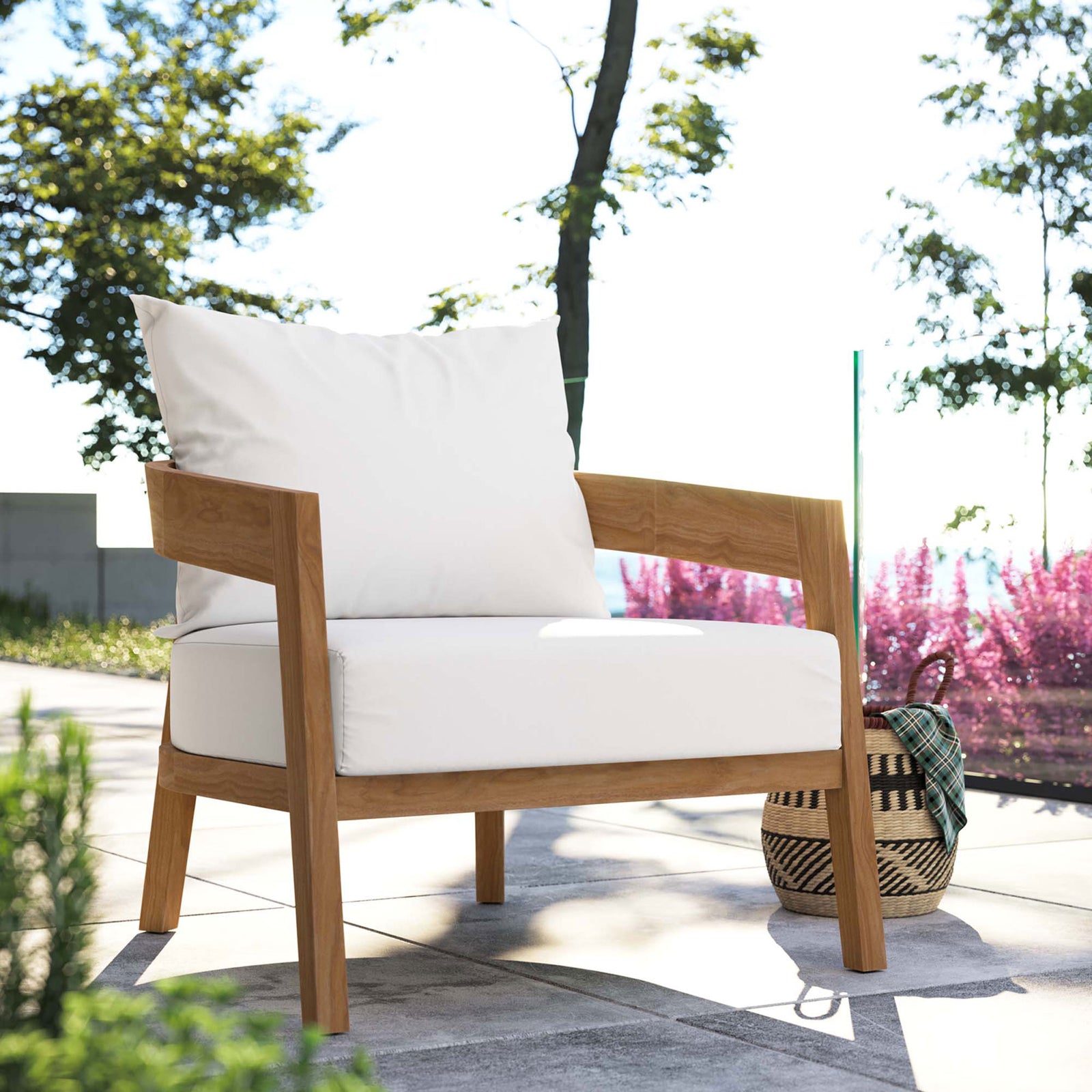 White cushioned teak patio armchair arranged on a scenic terrace overlooking water and flowering borders || EEI-5602-NAT-WHI || front_angle_room