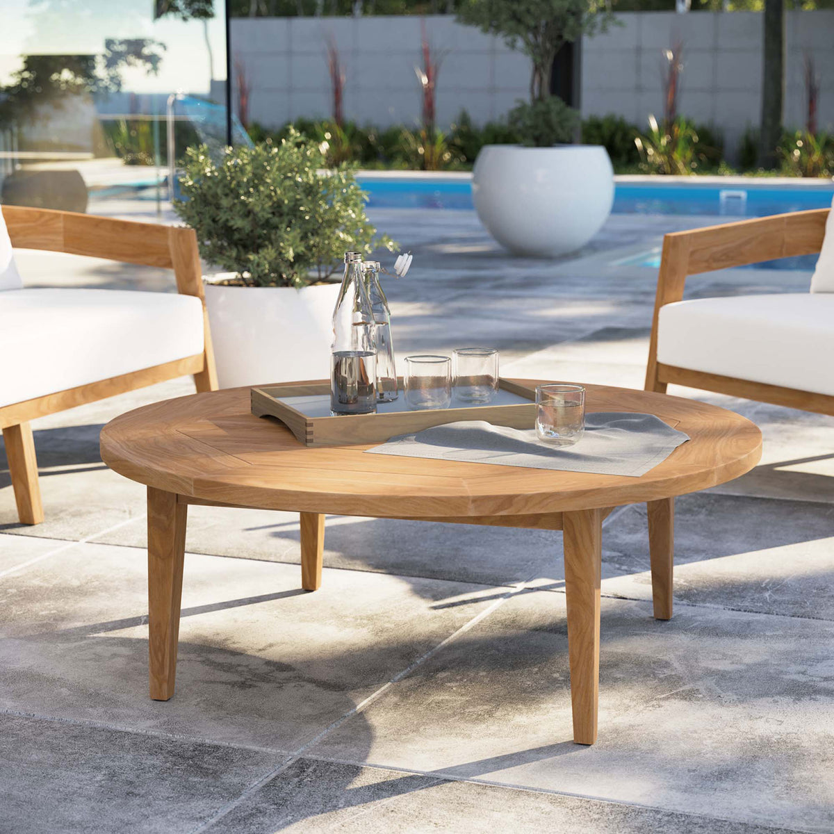 Round teak outdoor coffee table anchoring a modern poolside lounge seating area || EEI-5603-NAT || front_angle_room