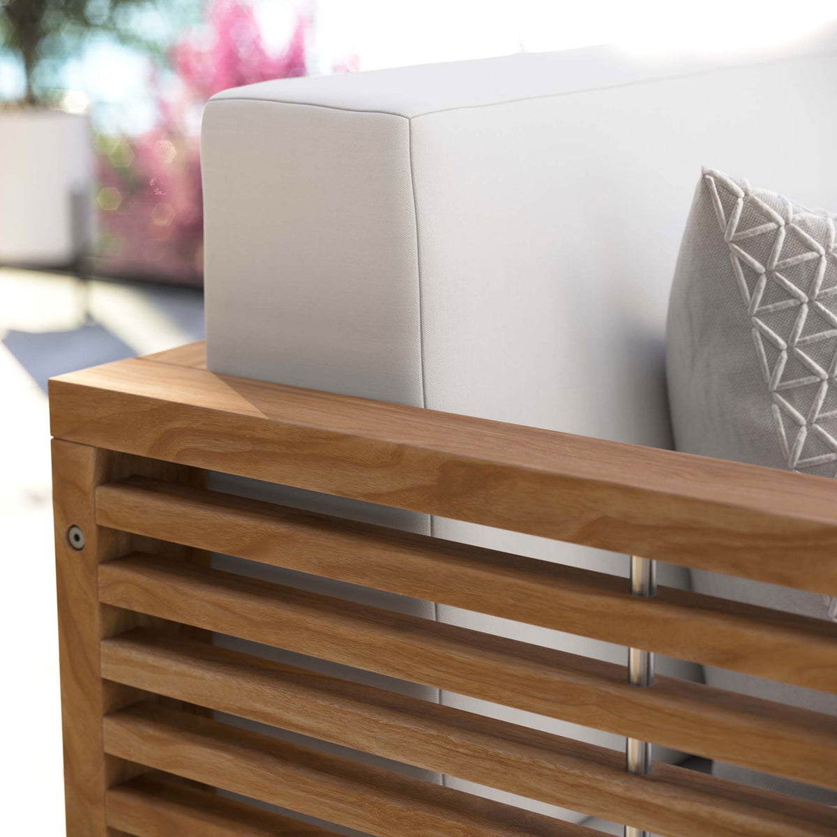 Outdoor close-up of the white loveseat cushion and teak armrest accented with a patterned throw pillow. || EEI-5605-NAT-WHI || detail_room