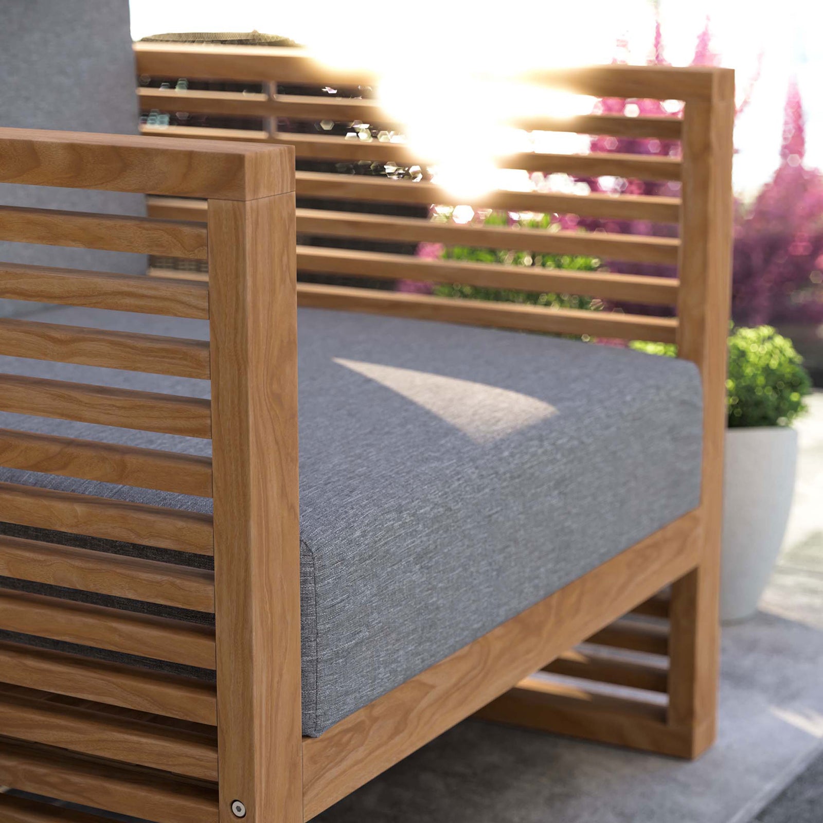Teak armrest and gray cushion of the Carlsbad armchair catching warm patio sunlight. || EEI-5606-NAT-GRY || detail_room