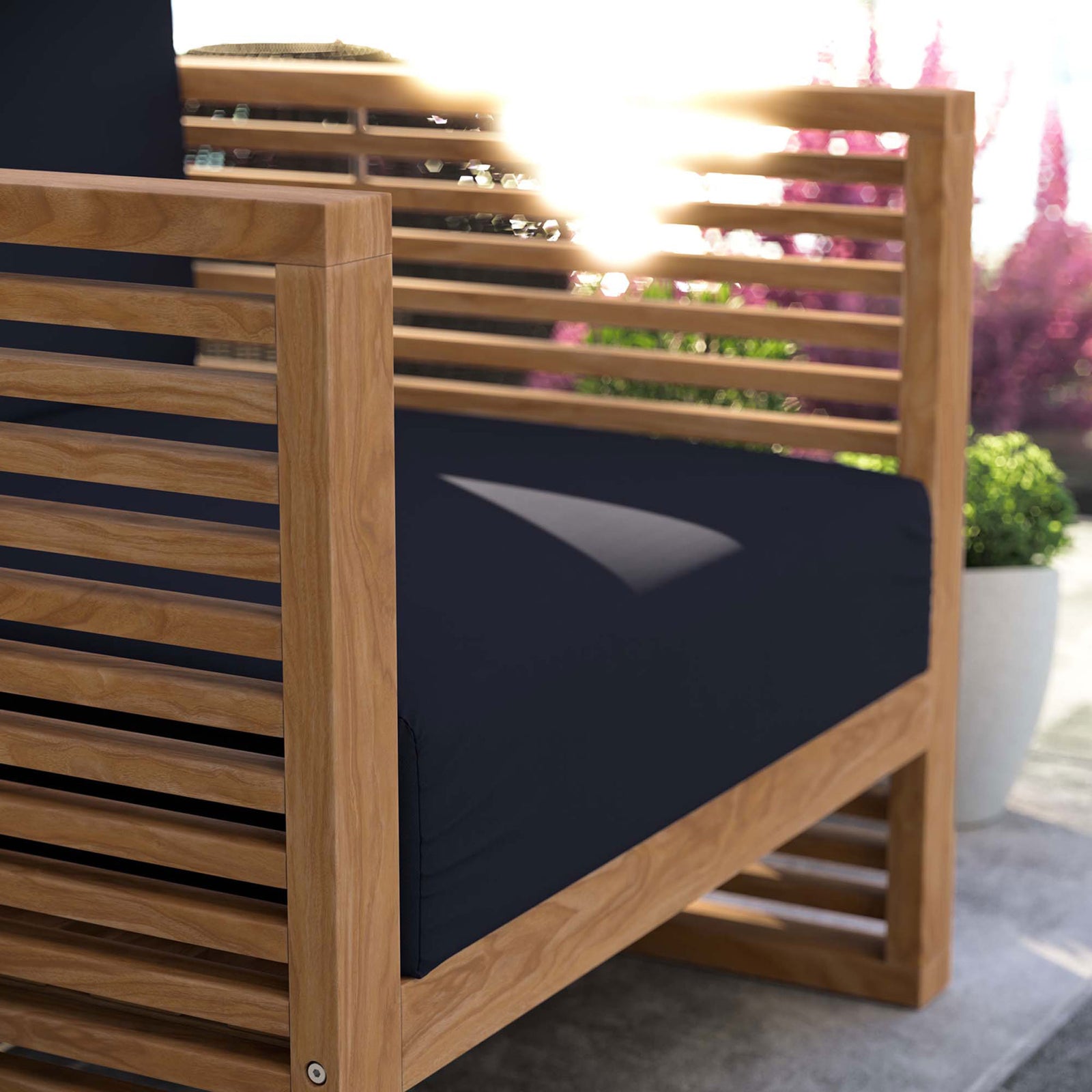 Teak armrest and navy cushion of the Carlsbad armchair glowing in warm outdoor sunlight. || EEI-5606-NAT-NAV || detail_room