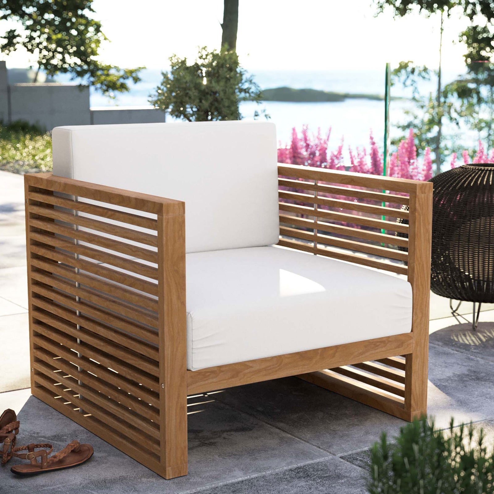 Carlsbad teak outdoor armchair with white cushions styled on a patio with lush coastal views. || EEI-5606-NAT-WHI || front_angle_room