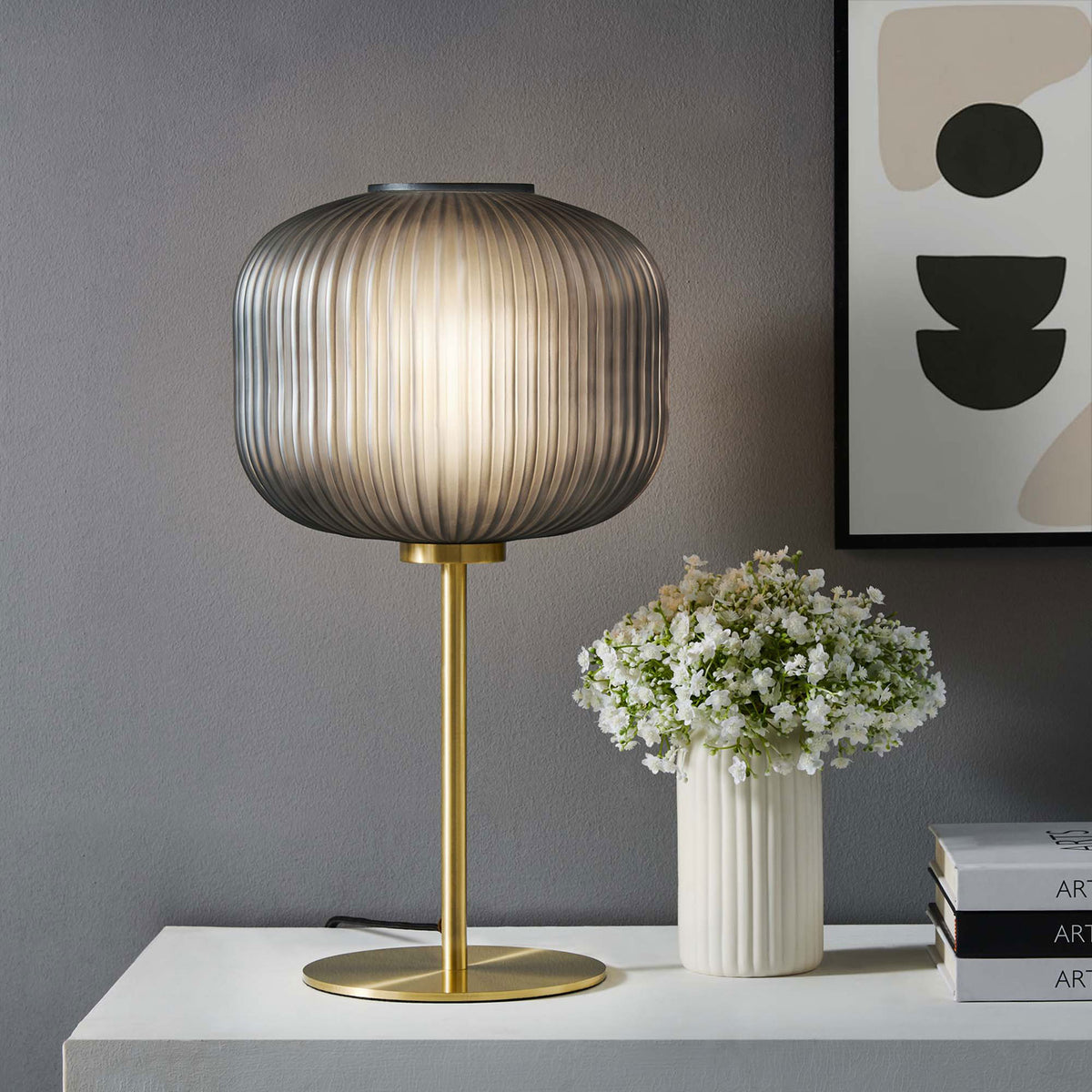 Smoked glass globe table lamp casting a warm ambient glow beside flowers and modern artwork || EEI-5622-BLK-SBR || front_on_room