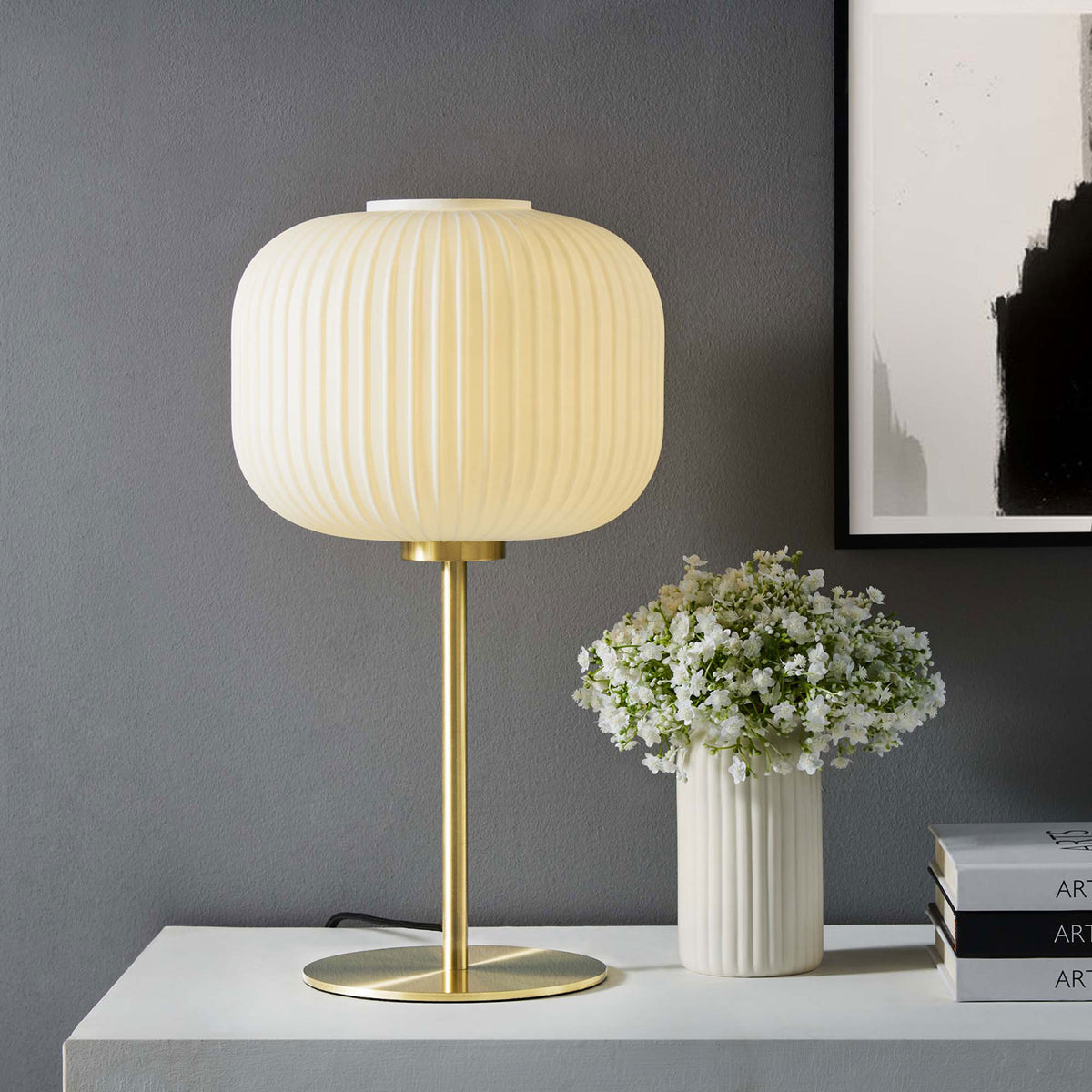 White glass globe table lamp glowing warmly beside flowers and framed modern artwork || EEI-5622-WHI-SBR || front_on_room