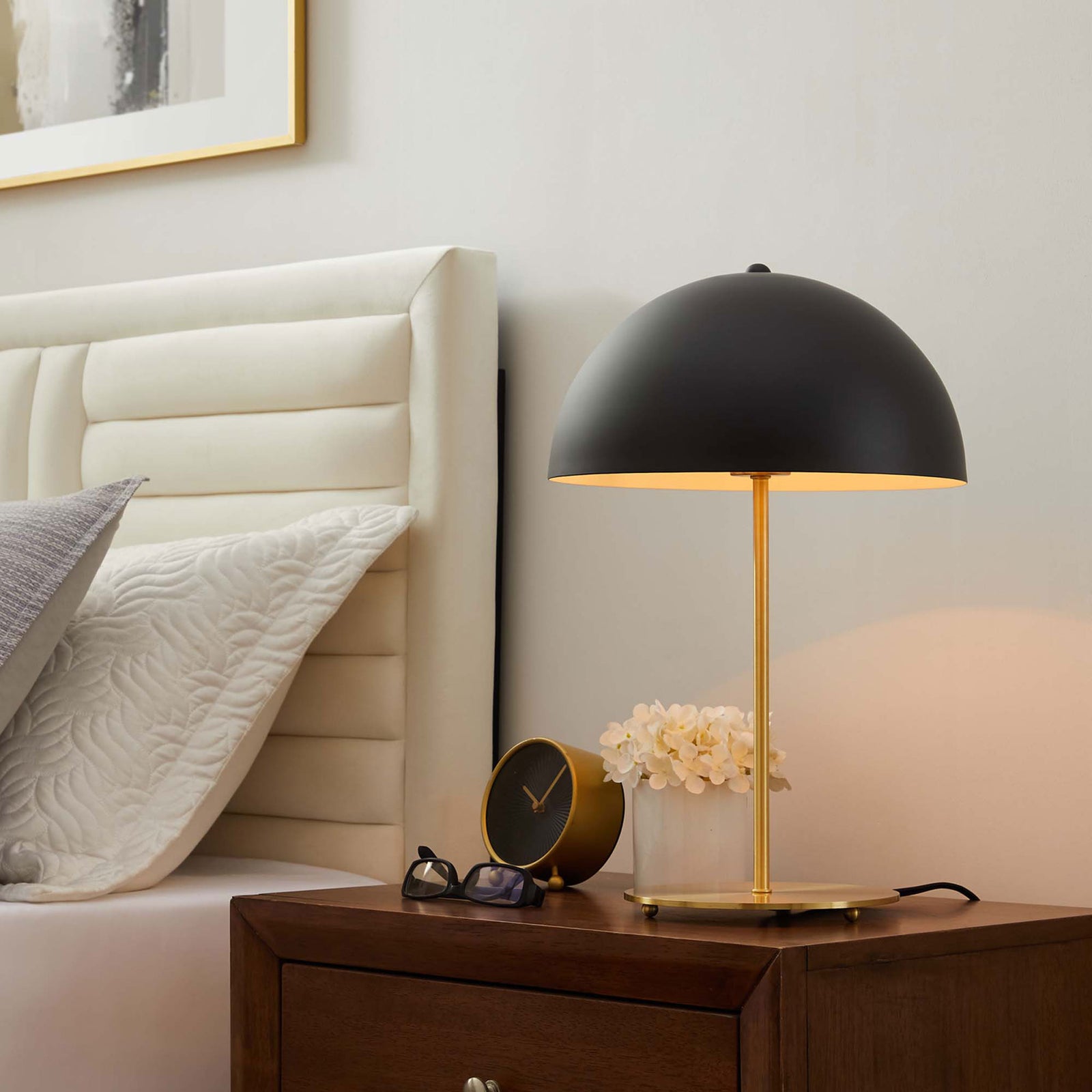 Black dome lamp casting a warm bedside glow over satin brass accents in a modern bedroom || EEI-5629-BLK-SBR || front_angle_on_room