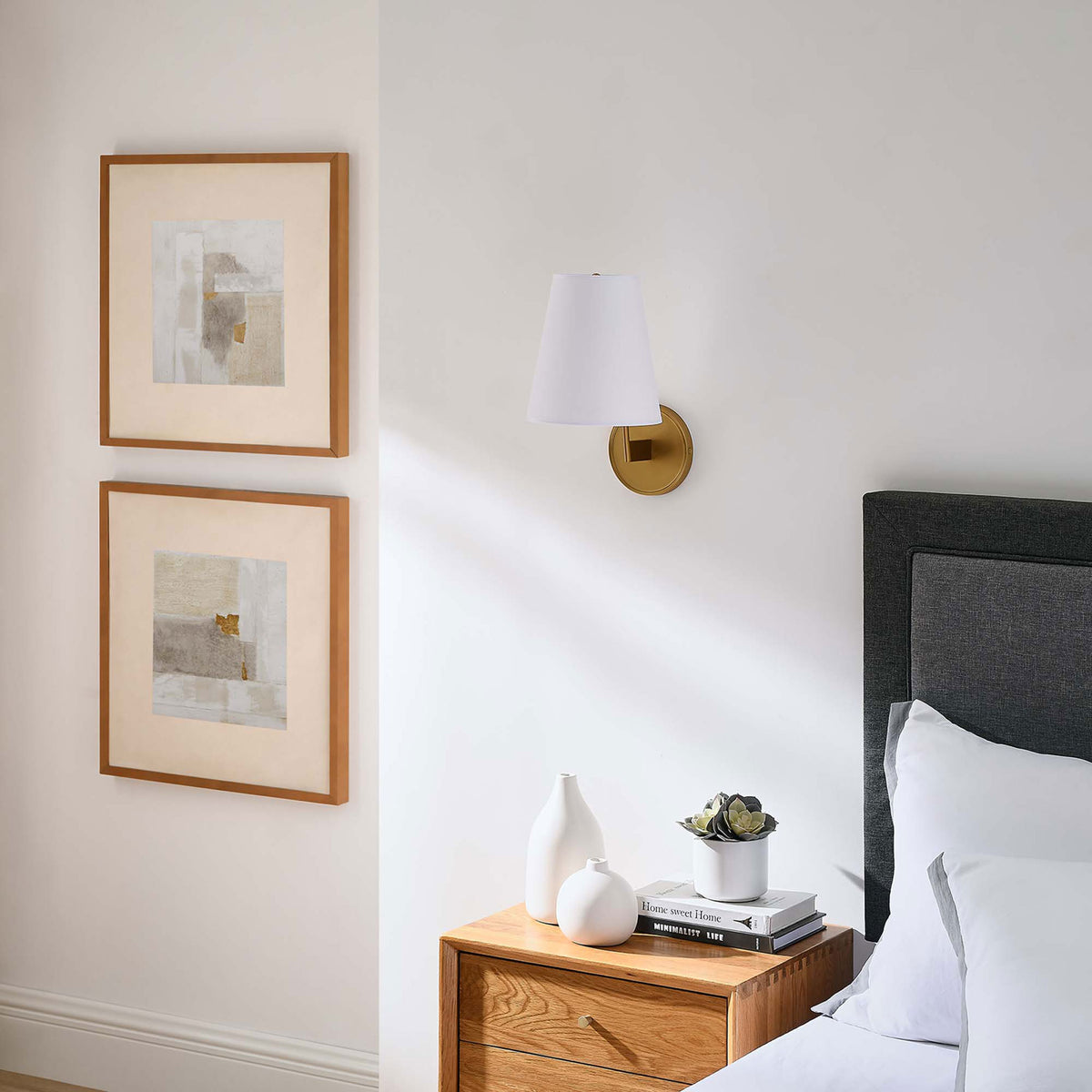 Satin brass wall sconce adding subtle metallic accent and soft contrast on a white bedroom wall. || EEI-5643-WHI-SBR || front_angle_room
