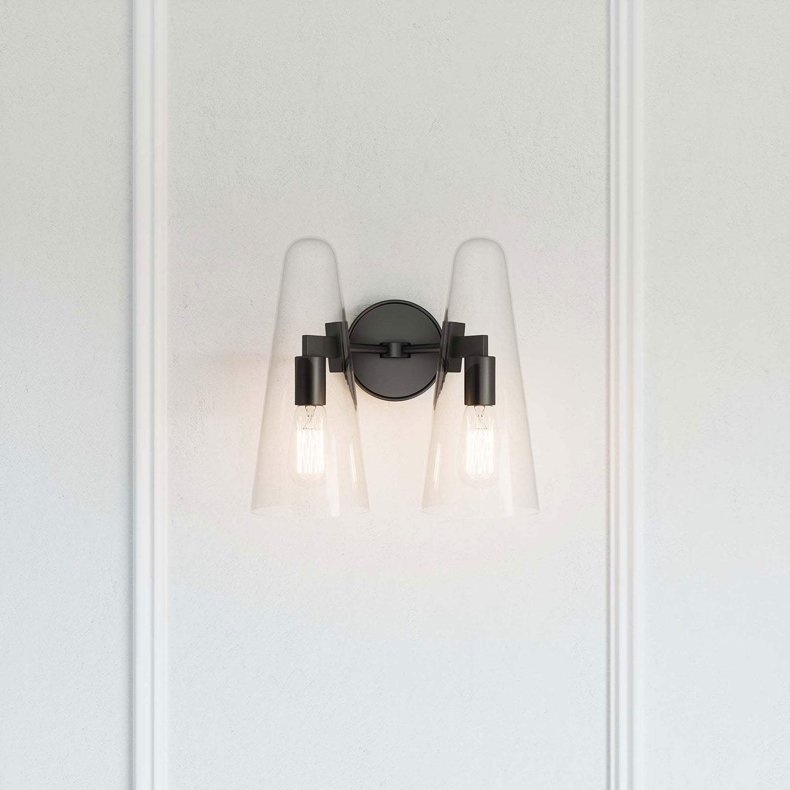Beacon black 2-light wall sconce casting a warm glow against a paneled white wall || EEI-5646-CLR-BLK || front_on_room
