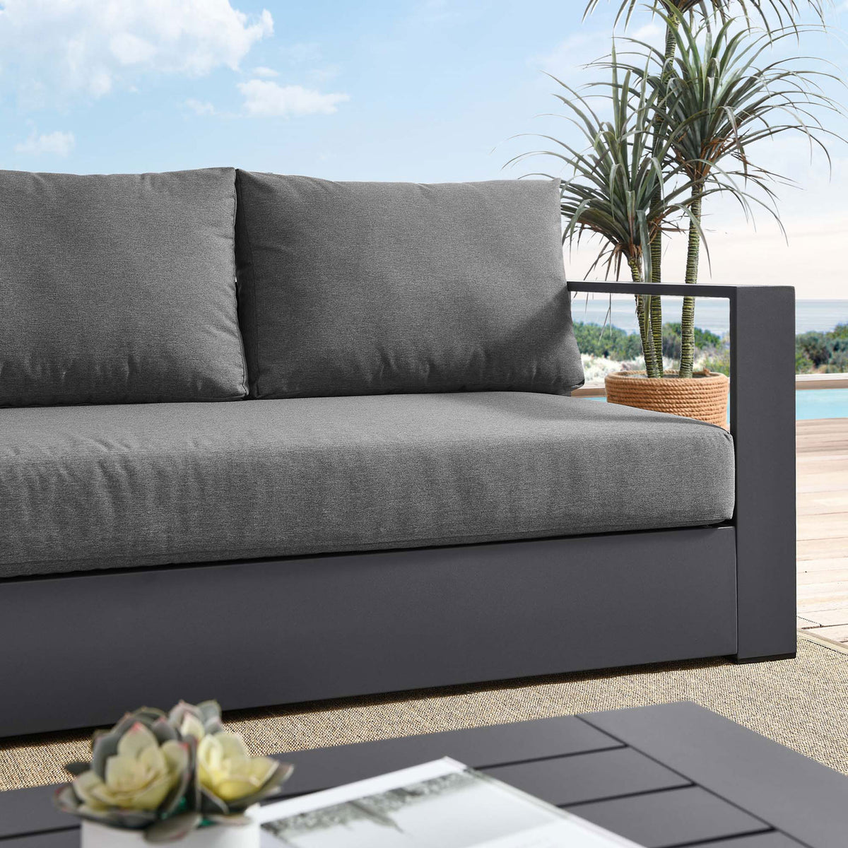 Close lifestyle view of the Tahoe sofa, pairing dark gray cushions with a charcoal frame on the patio. || EEI-5676-GRY-CHA || detail_room