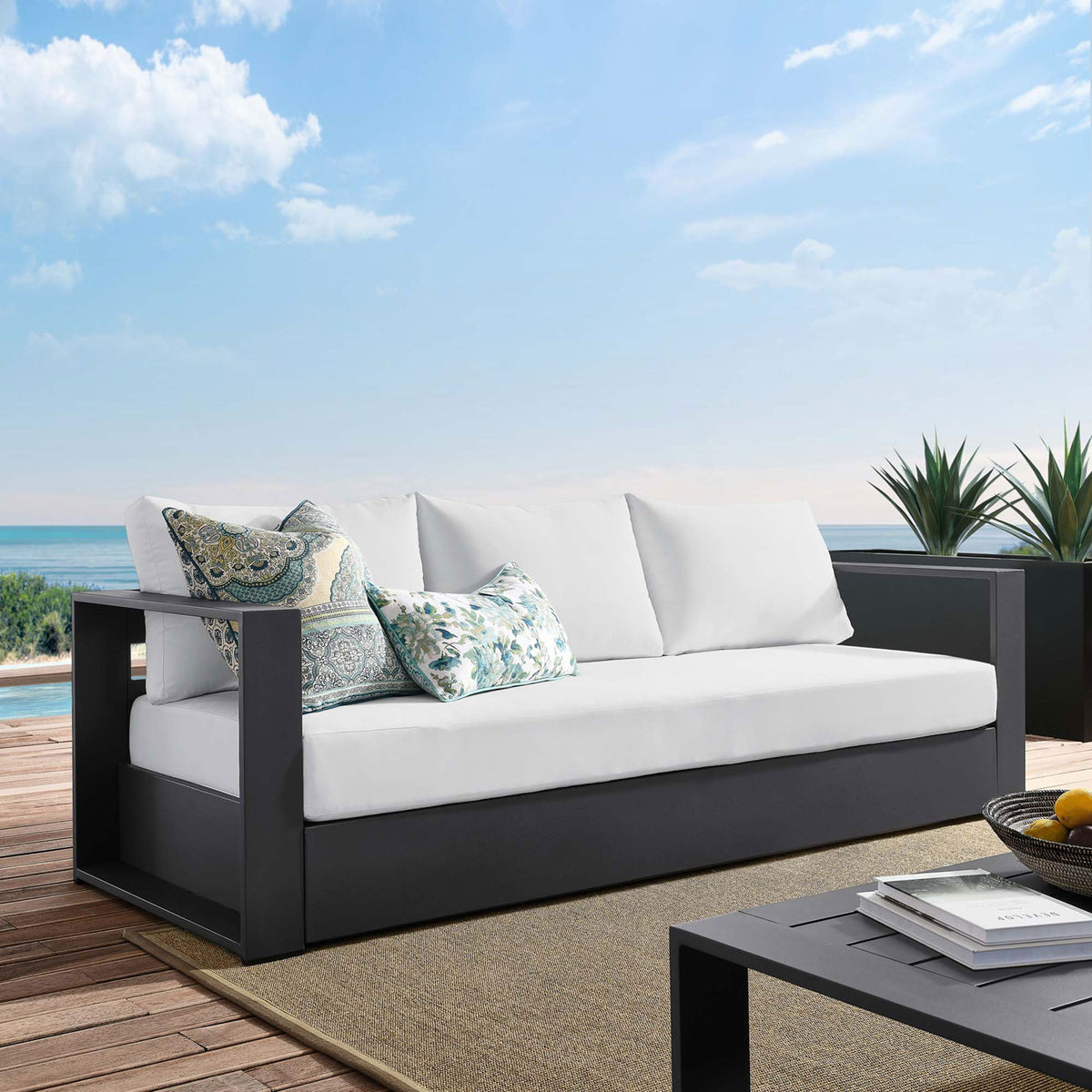 Tahoe outdoor sofa with charcoal frame and white cushions styled on a breezy coastal deck. || EEI-5676-GRY-WHI || front_angle_room