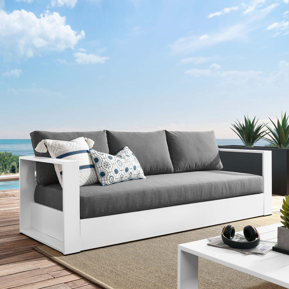 Tahoe outdoor sofa with white frame and charcoal cushions styled seaside with patterned pillows. || EEI-5676-WHI-CHA || front_angle_room