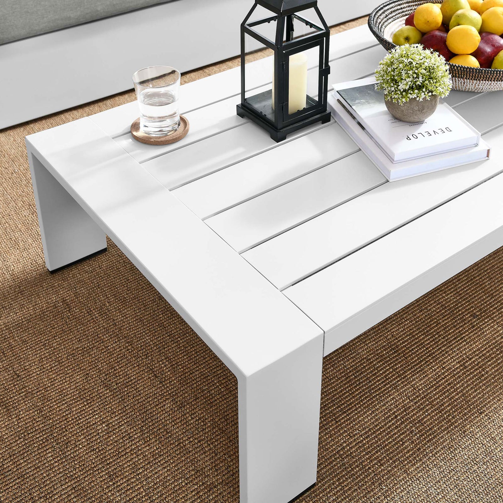 White aluminum coffee table styled with decor on an outdoor rug beside patio seating || EEI-5677-WHI || front_angle_room