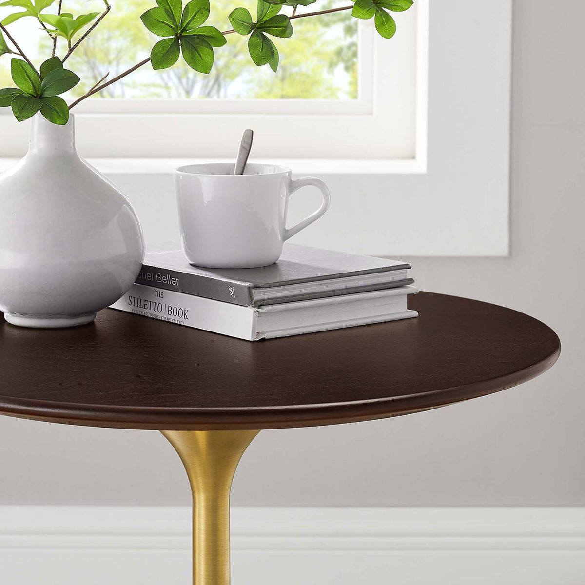 Styled tabletop close up with vase, coffee cup, and books on the warm wood grain surface || EEI-5684-GLD-CHE || detail_room
