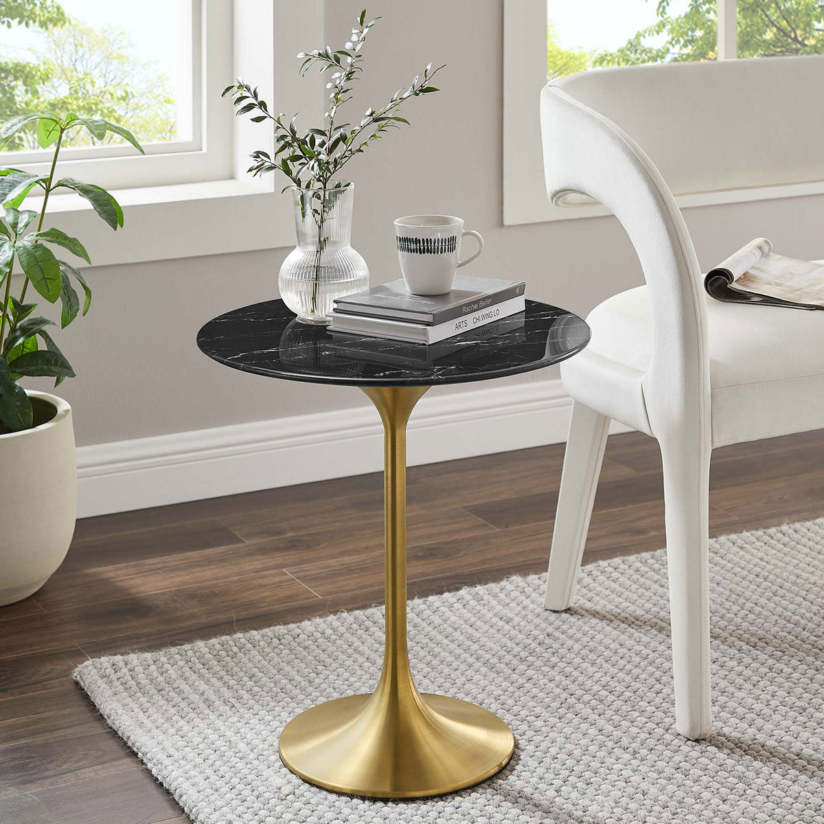Round black faux marble and gold pedestal side table beside a modern white chair in a bright room || EEI-5685-GLD-BLK || front_angle_room