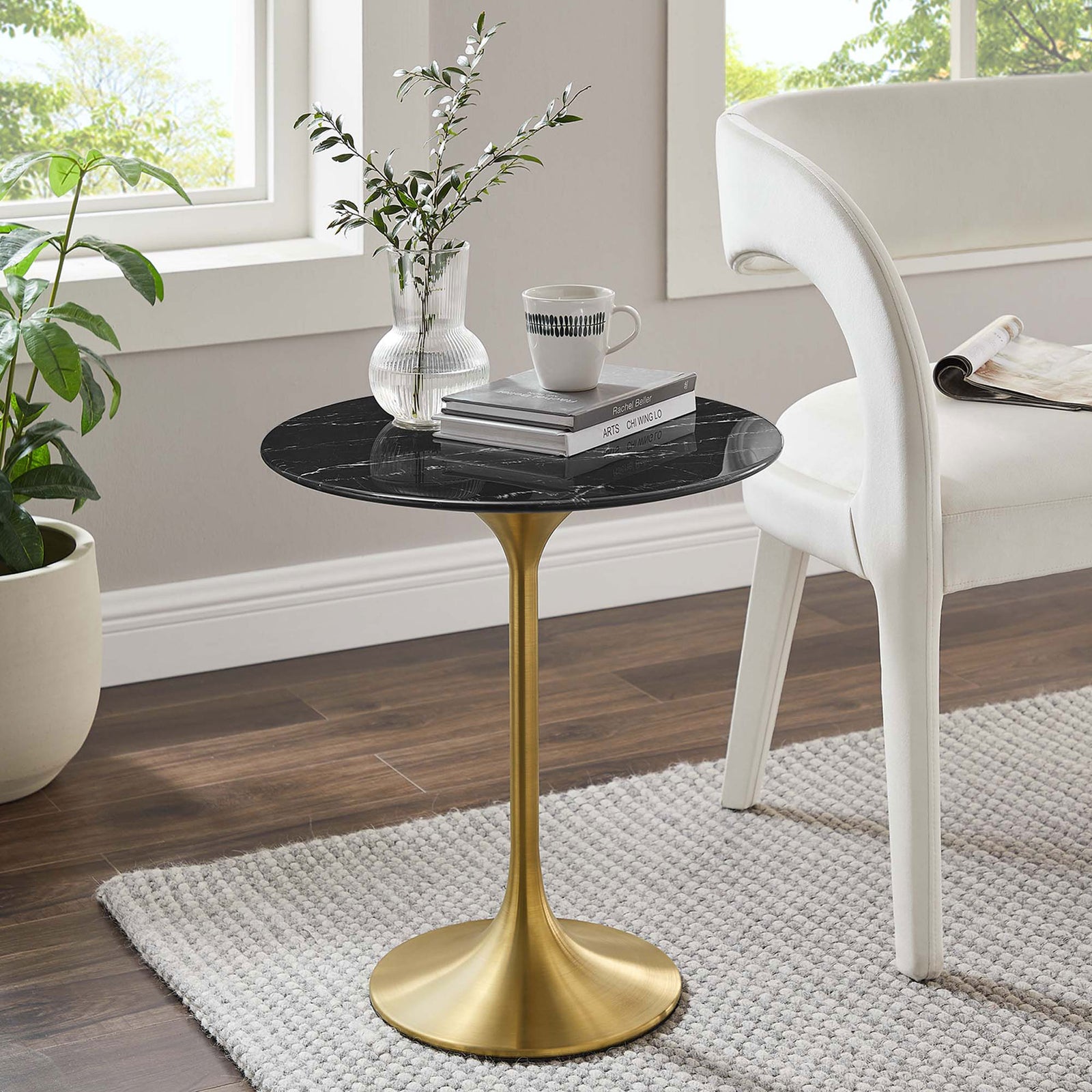 Round black faux marble and gold pedestal side table beside a modern white chair in a bright room || EEI-5685-GLD-BLK || front_angle_room