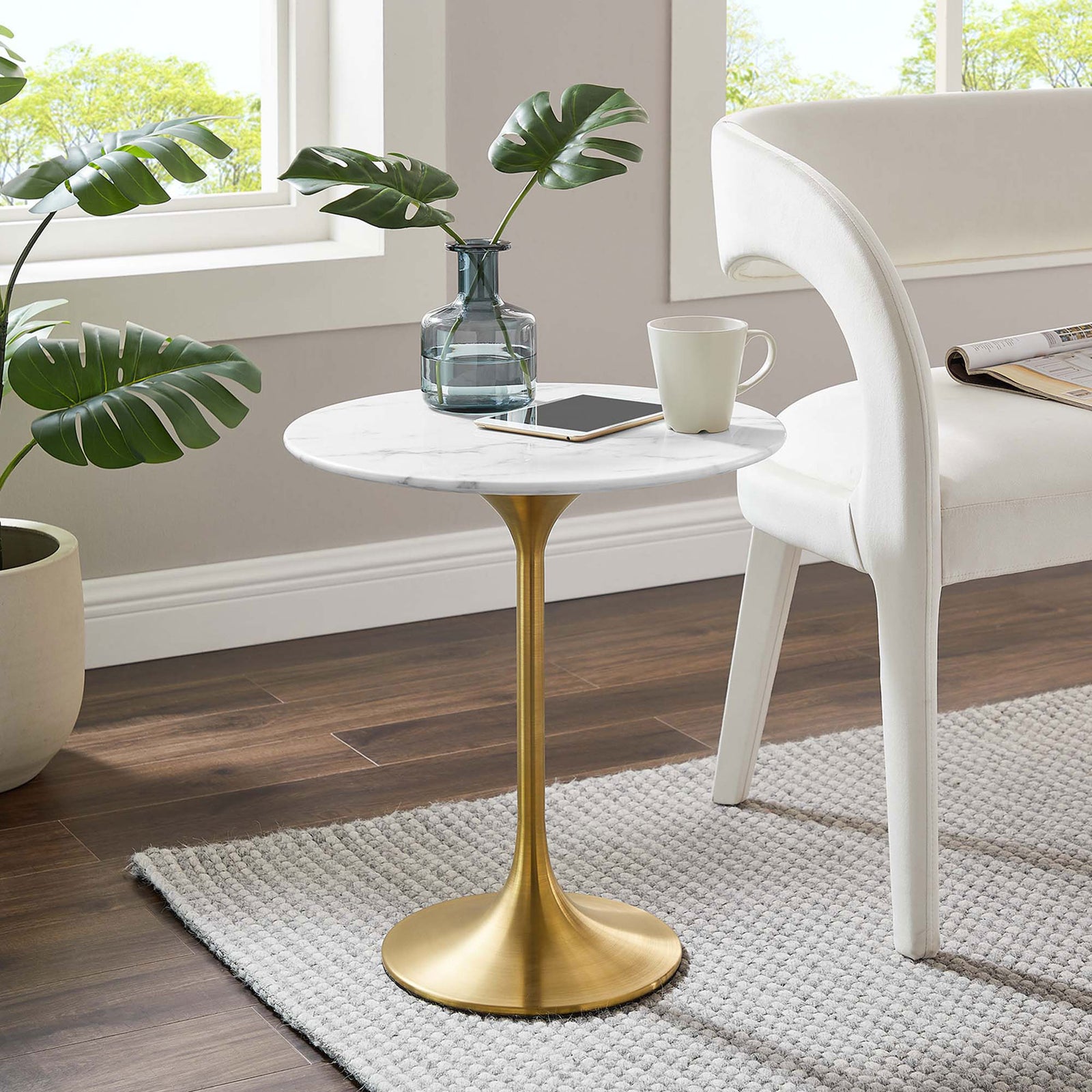 Lippa round faux marble side table with gold pedestal base styled beside a modern chair in a bright living room || EEI-5685-GLD-WHI || front_angle_room