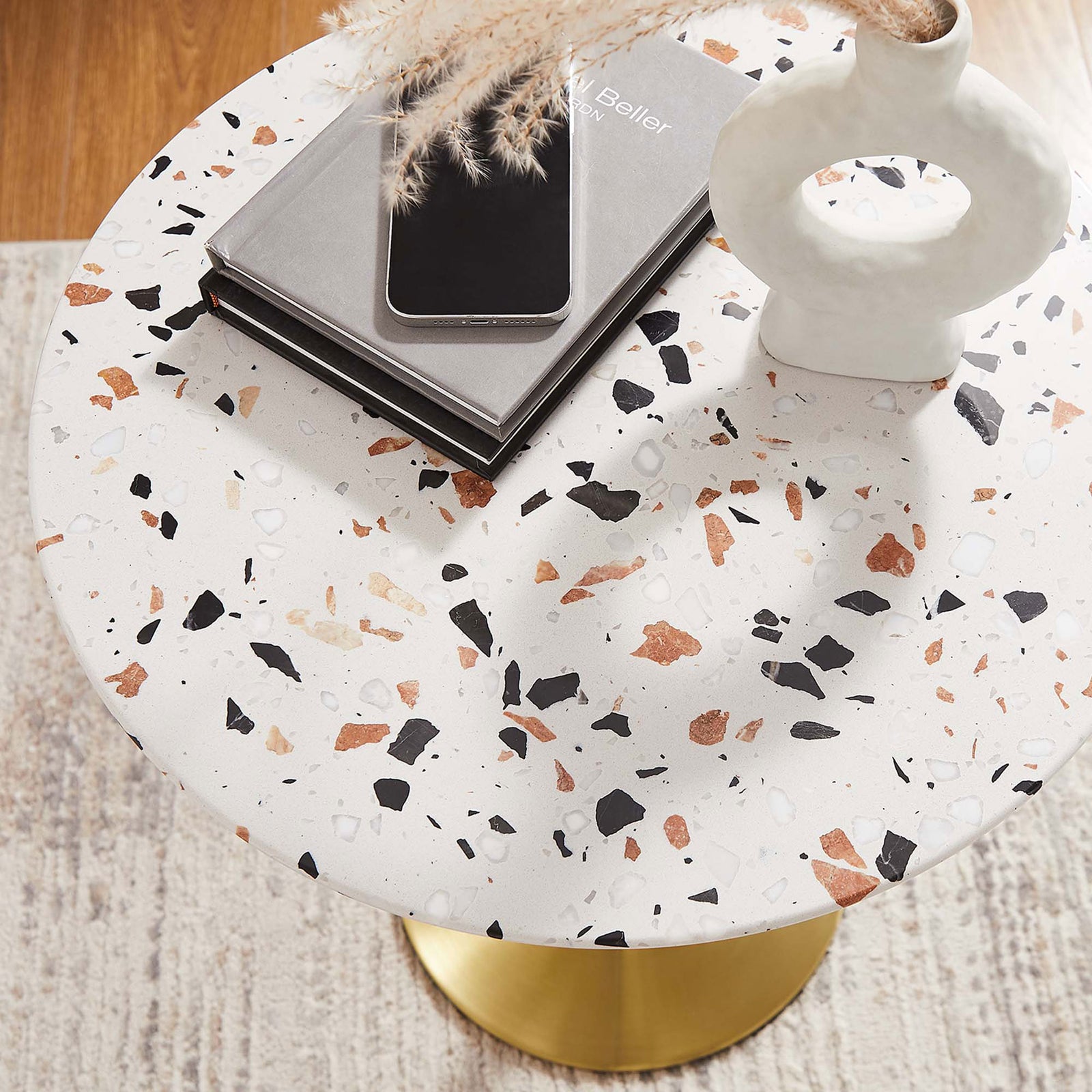 Styled terrazzo side table with books, vase, and phone atop the speckled white surface || EEI-5687-GLD-TER || detail_room