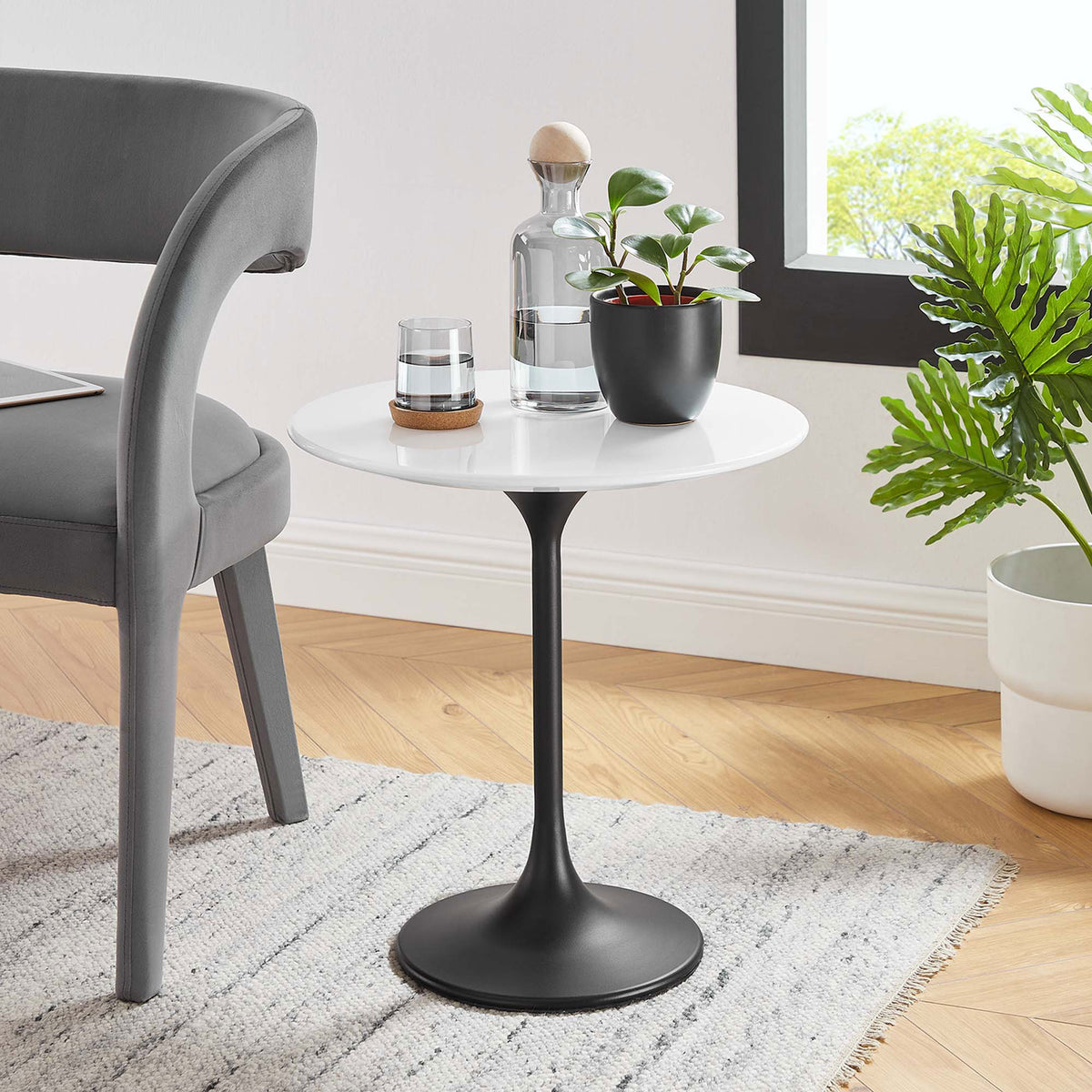 Round side table with white top and black base styled next to a modern accent chair || EEI-5688-BLK-WHI || front_angle_room